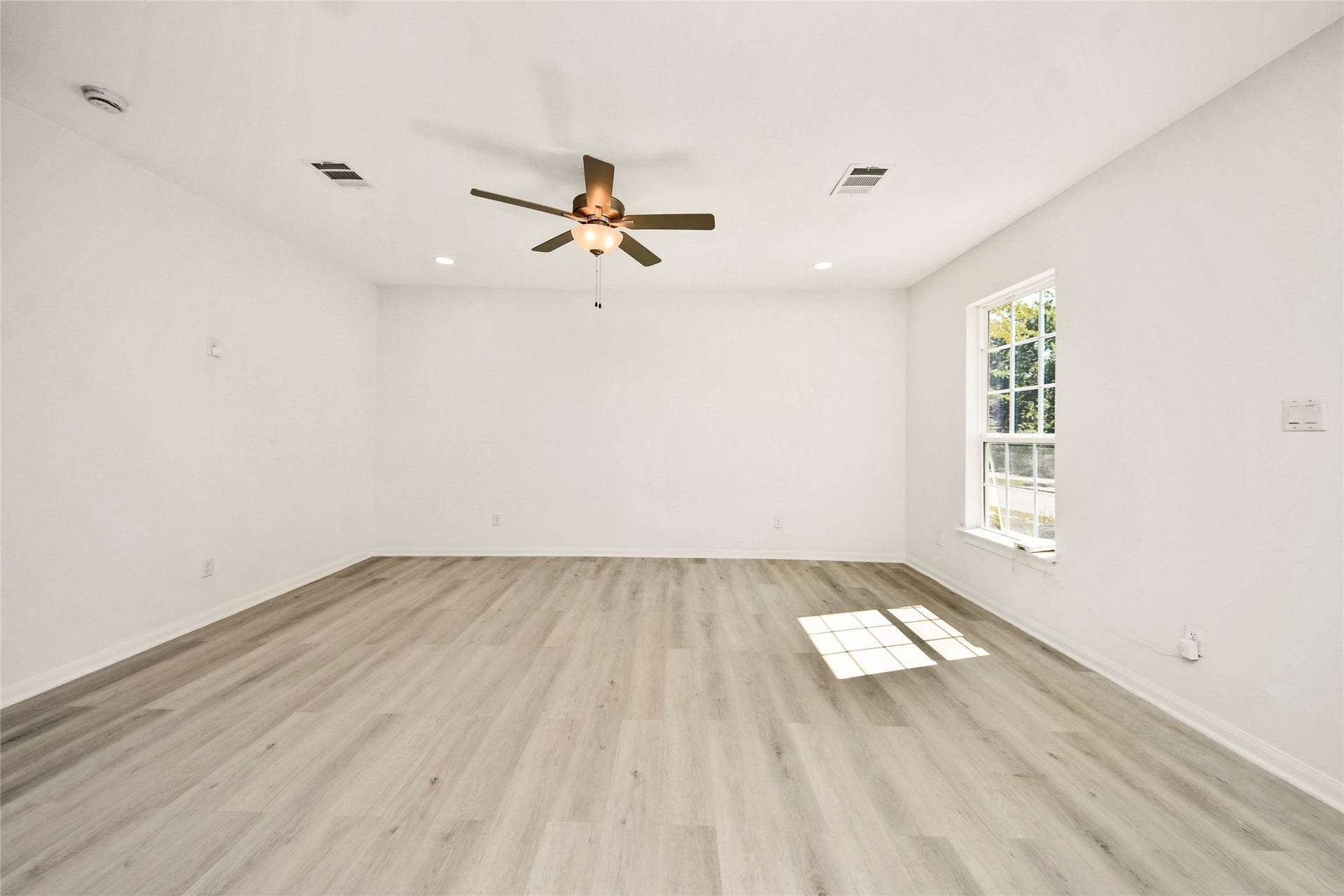 4615 Collingsworth Street, #AB, Houston, TX 77026 Spacious and bright living area featuring new laminate flooring, a modern ceiling fan, and abundant natural light from a large window.