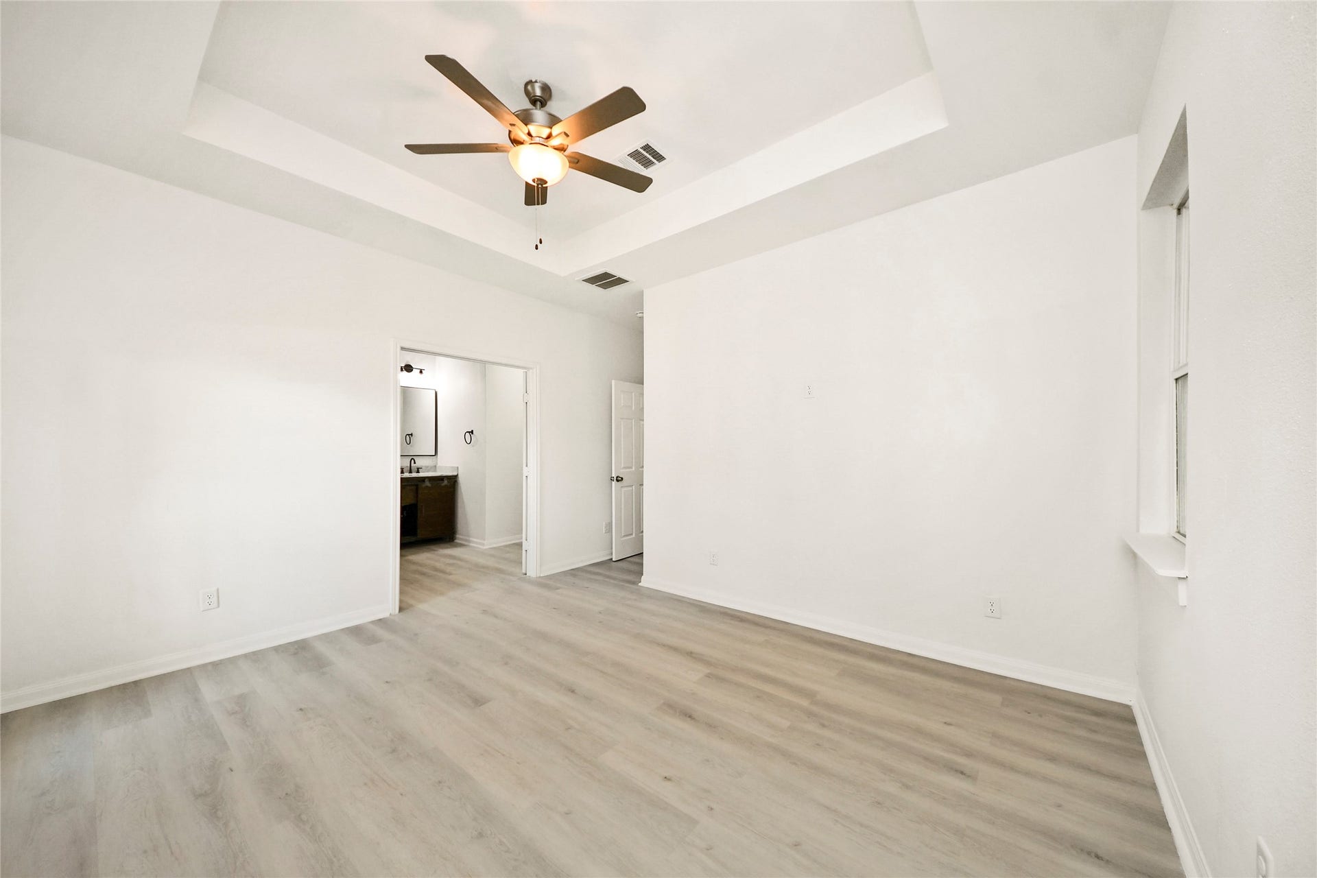 4615 Collingsworth Street, #AB, Houston, TX 77026 Spacious bedroom with elegant tray ceiling, ceiling fan, and light wood flooring, leading to a modern ensuite bathroom.