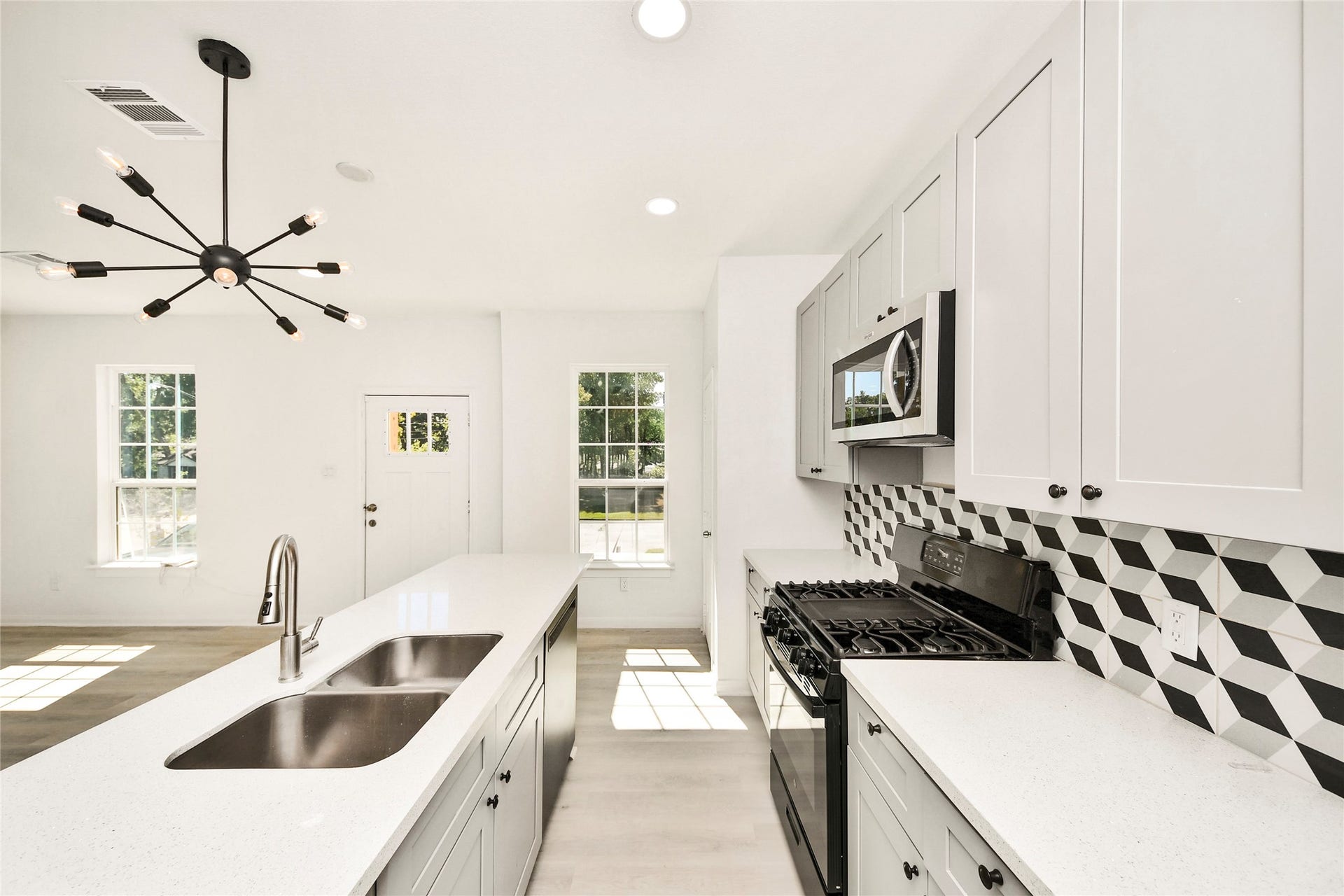 4615 Collingsworth Street, #AB, Houston, TX 77026 Modern kitchen with sleek white cabinetry, geometric backsplash, and a central island featuring a double sink. Natural light floods the space, highlighting the contemporary pendant lighting and stainless steel appliances.