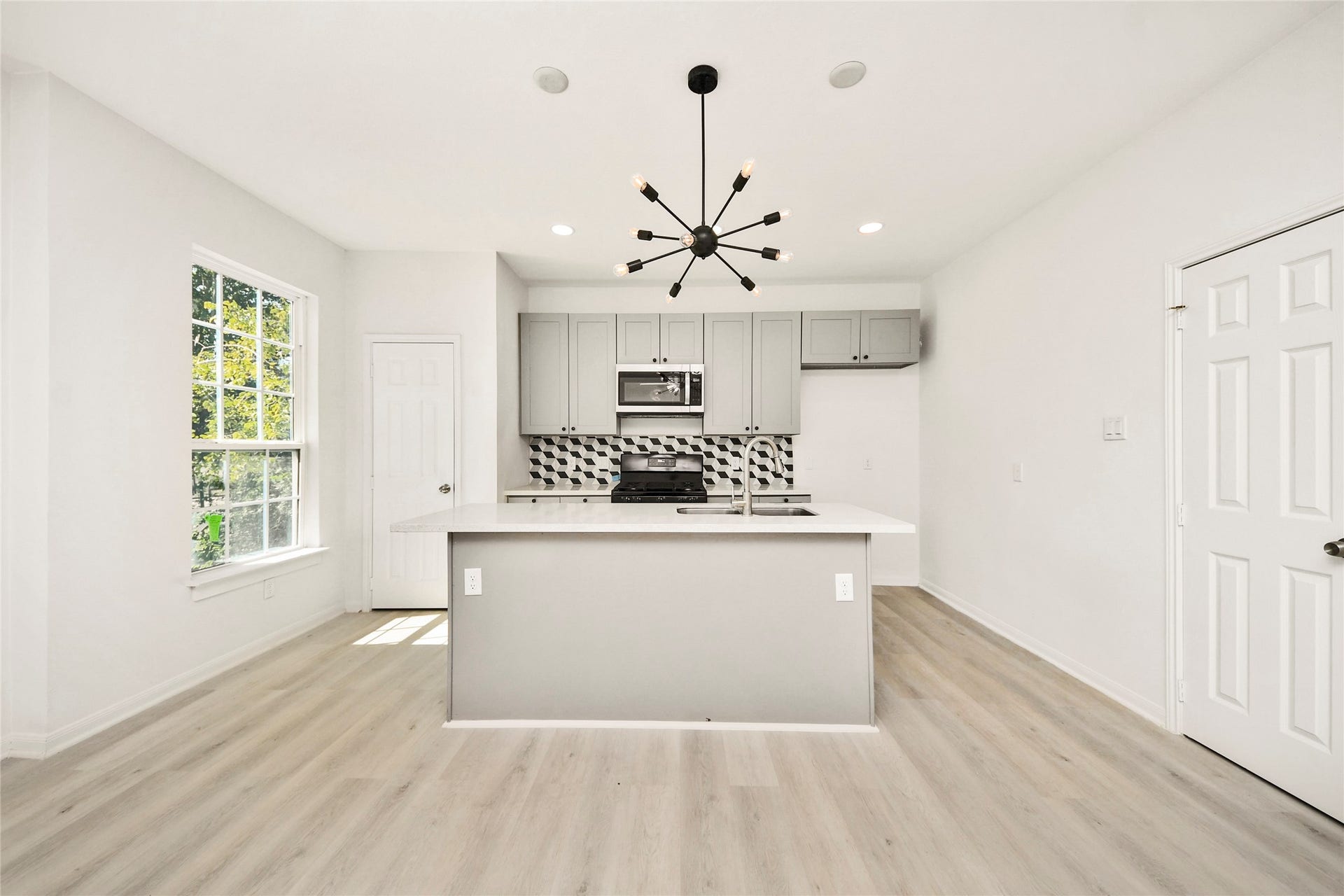 4615 Collingsworth Street, #AB, Houston, TX 77026 Bright and modern kitchen featuring sleek gray cabinetry, a stylish geometric backsplash, and a central island with a contemporary light fixture, all enhanced by natural light from large windows.