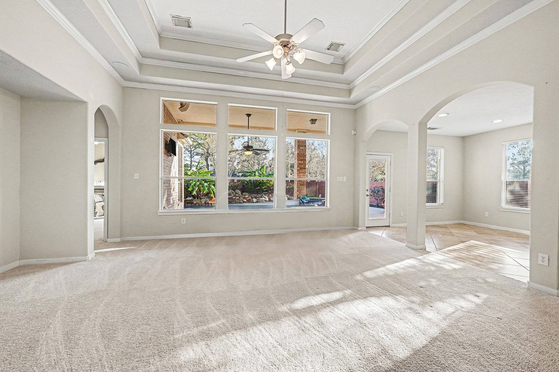 This shows another view of family room with no furniture featuring the wall of windows, arches, tray ceiling and  showing the backyard santuary.