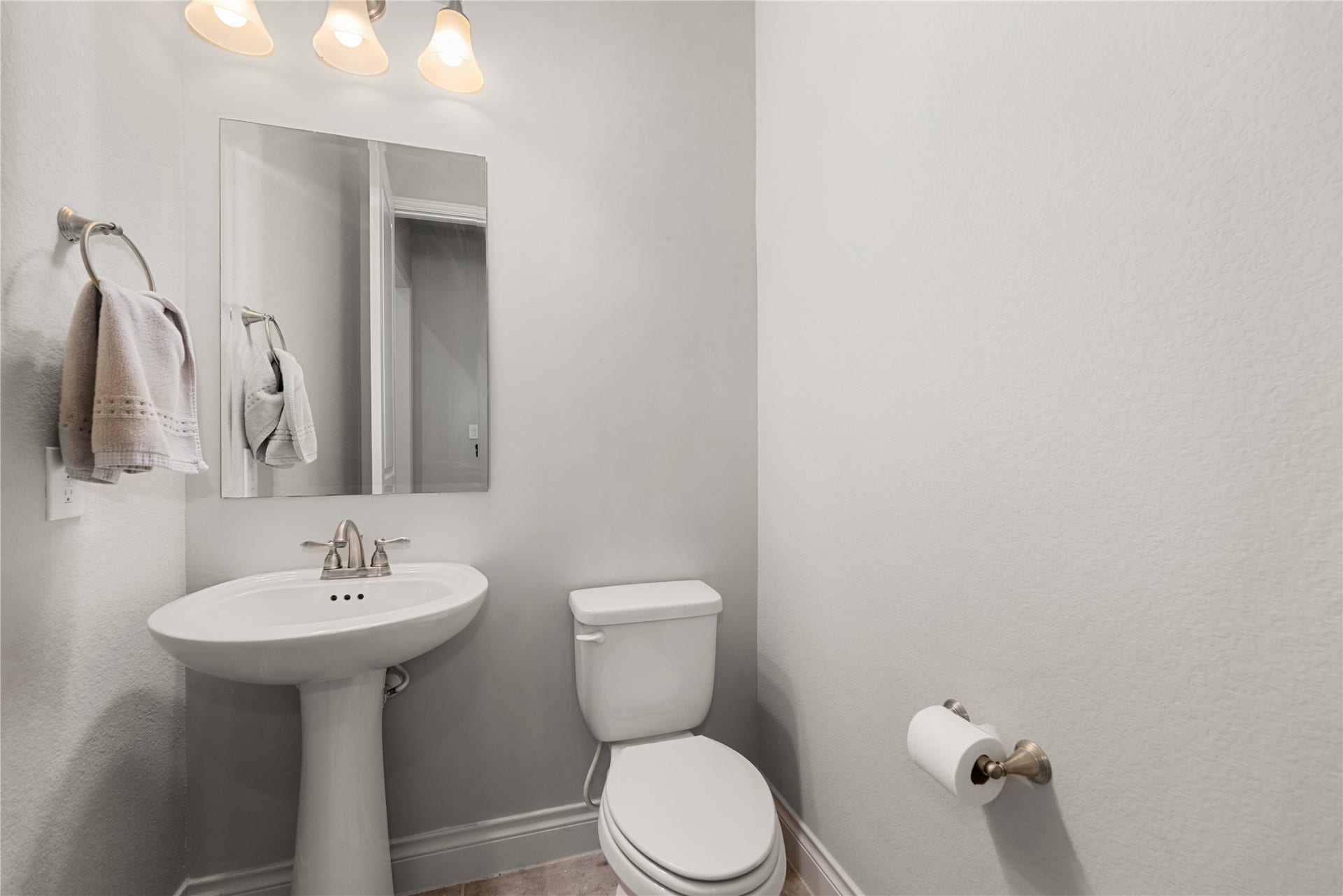 4103 August Light Court, Fulshear, TX 77441 A classic, white ceramic pedestal sink anchors the room, pairing perfectly with a polished chrome faucet for a timeless, space-saving design. A sleek, frameless rectangular vanity mirror sits beneath a modern glass shade vanity light fixture, flooding the corner with a bright, welcoming glow.