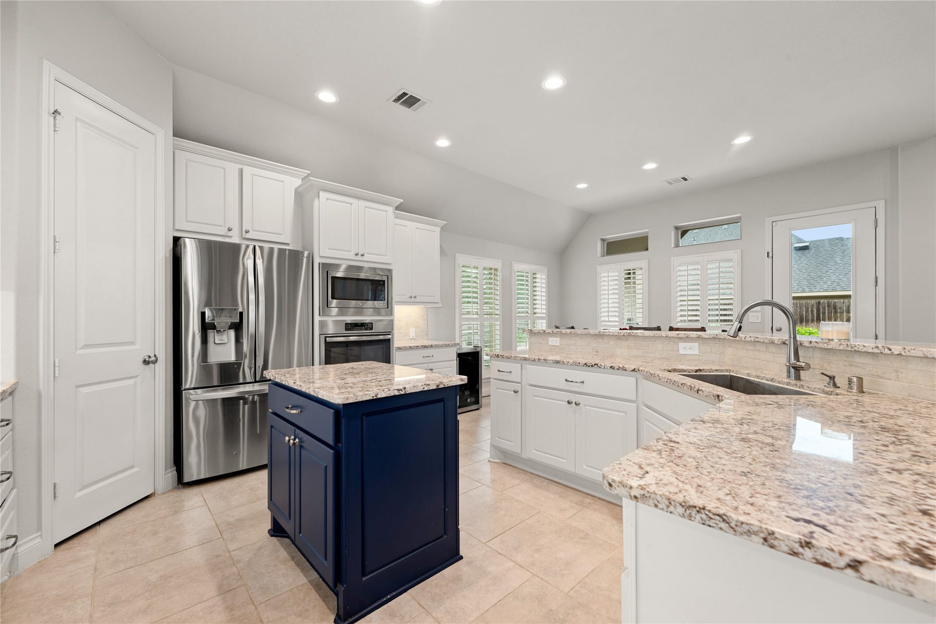 4103 August Light Court, Fulshear, TX 77441 A massive, sweeping wrap-around island serves as the ultimate gathering spot, complete with an under-mount stainless steel sink, a premium gooseneck faucet, and expansive granite countertops. Bright white perimeter cabinetry contrasts beautifully with the navy-blue central island, adding a sophisticated pop of color to the crisp design.