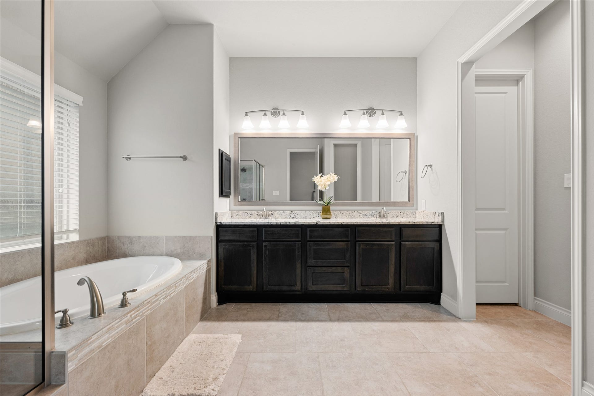 4103 August Light Court, Fulshear, TX 77441 An expansive, dark-finished double vanity serves as the striking anchor of the room, topped with pristine light solid-surface counters and equipped with dual undermount sinks. A sprawling, seamless mirror stretches above the vanity, brilliantly bouncing the light from a pair of modern multi-bulb vanity fixtures.