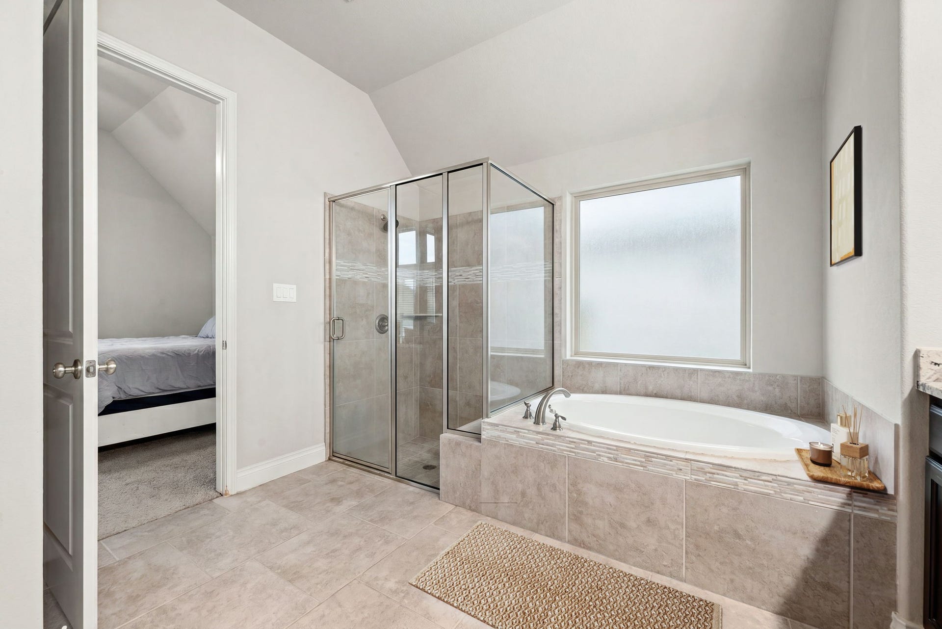 4103 August Light Court, Fulshear, TX 77441 To the side, a deep soaking tub and oversized walk-in shower wrapped in neutral stone-look tile sits tucked beneath a vaulted ceiling detail and a large picture window, offering the ultimate setup for relaxation.