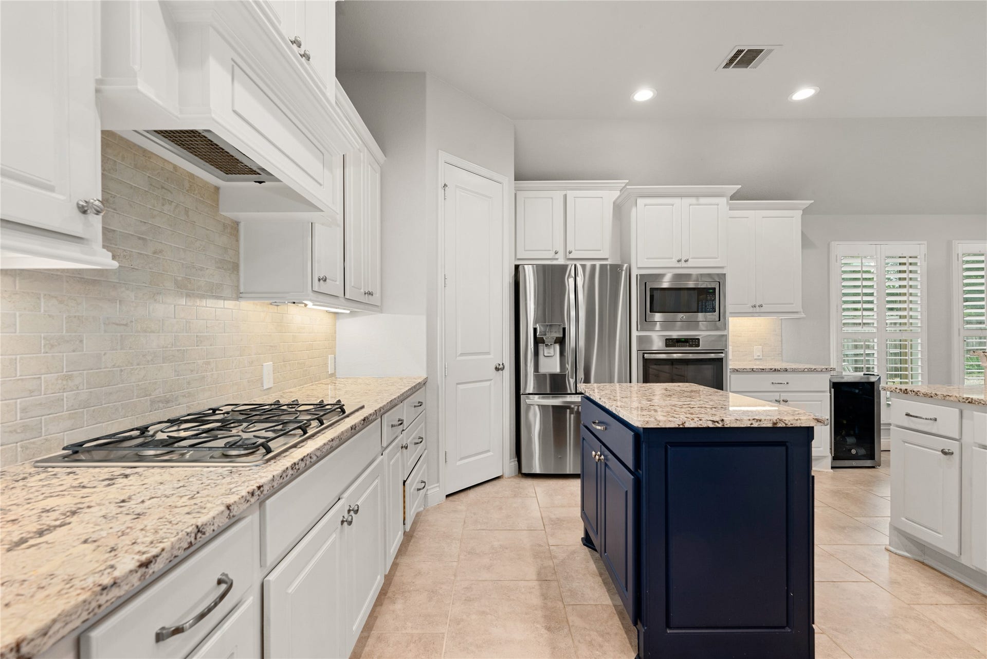 4103 August Light Court, Fulshear, TX 77441 This gourmet workspace features a built-in gas cooktop beautifully framed by a custom-styled vent hood and a sleek, neutral tile backsplash. Premium granite countertops offer sprawling prep space, illuminated by crisp recessed lighting and subtle under-cabinet accents. The thoughtful layout includes a spacious corner pantry for maximum storage and opens directly into the wider living areas, making it as practical for daily life as it is for grand entertaining.