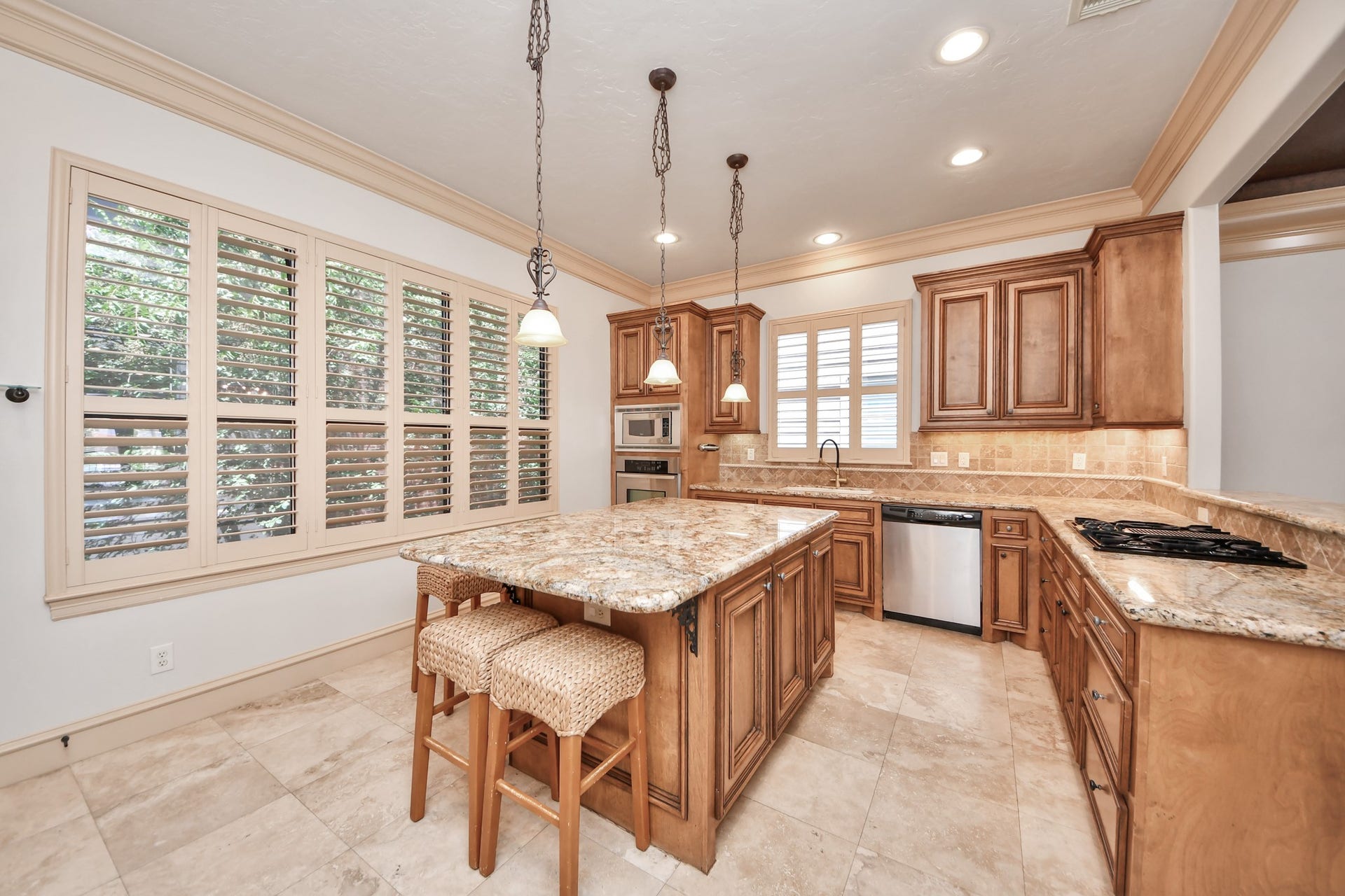 Elegant kitchen featuring a large granite island, rich wood cabinetry, and ample natural light from stylish plantation shutters.