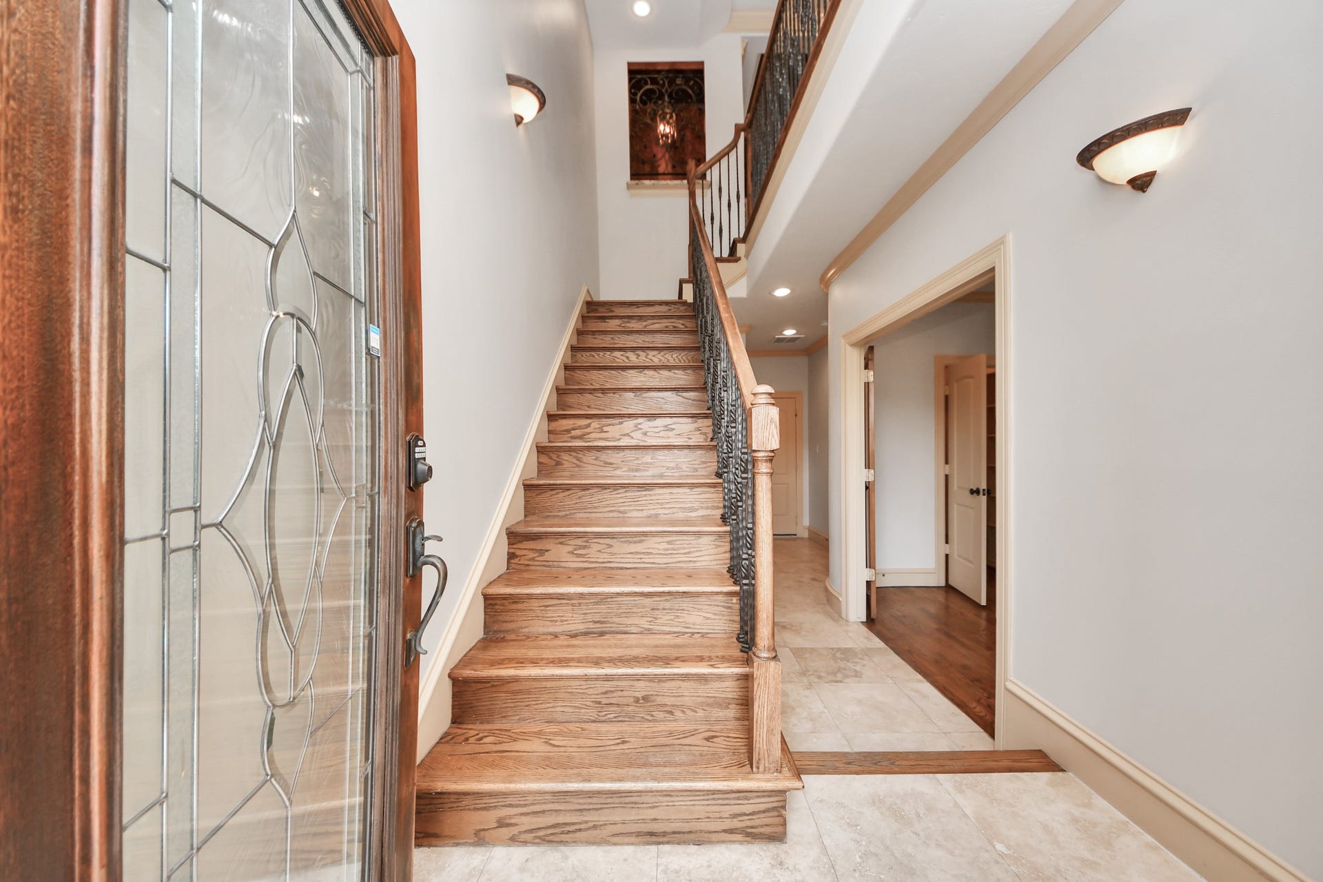 Elegant entryway featuring a striking wooden staircase with wrought iron balusters, and a beautifully detailed glass front door, leading into a spacious, light-filled hallway.