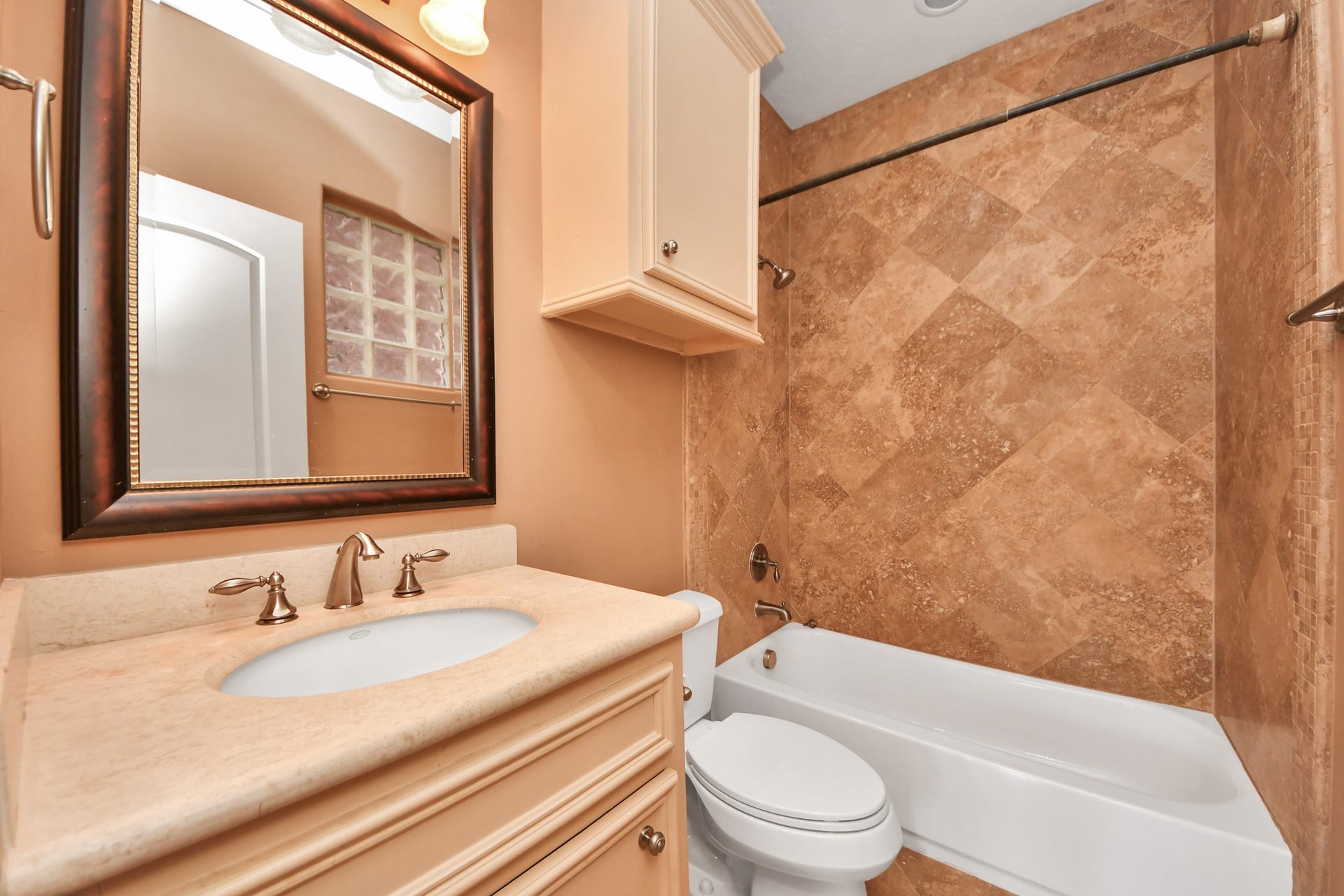 En-suite  first floor bathroom featuring a marble-topped vanity, framed mirror, and a tiled tub/shower with a sleek bronze fixture.
