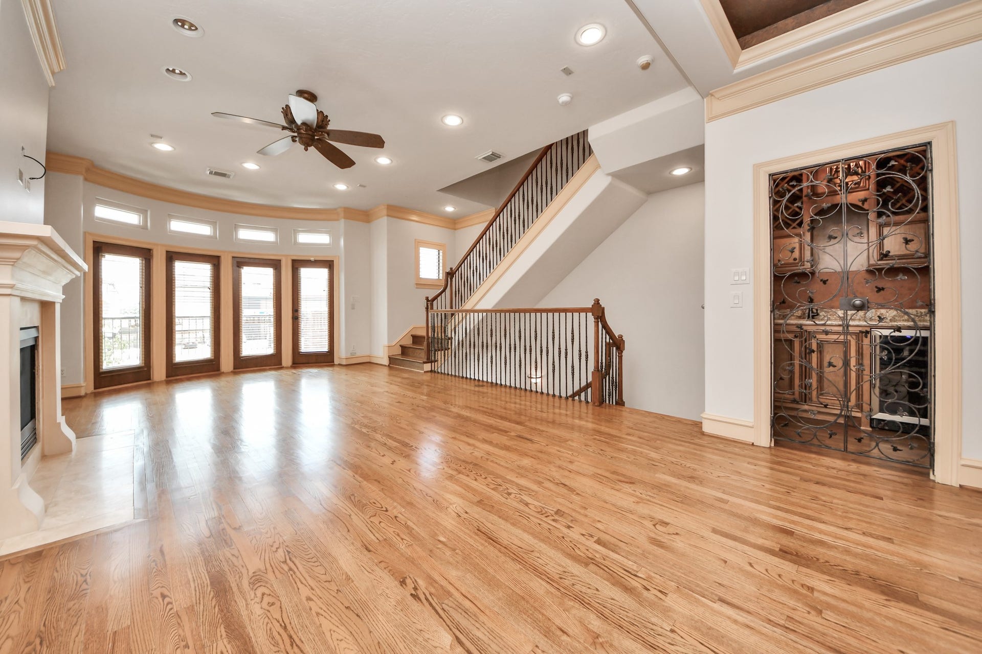 Spacious living area with elegant hardwood floors, a cozy fireplace, and abundant natural light from tall windows. A stylish staircase enhances the open layout, complemented by a charming built-in bar.