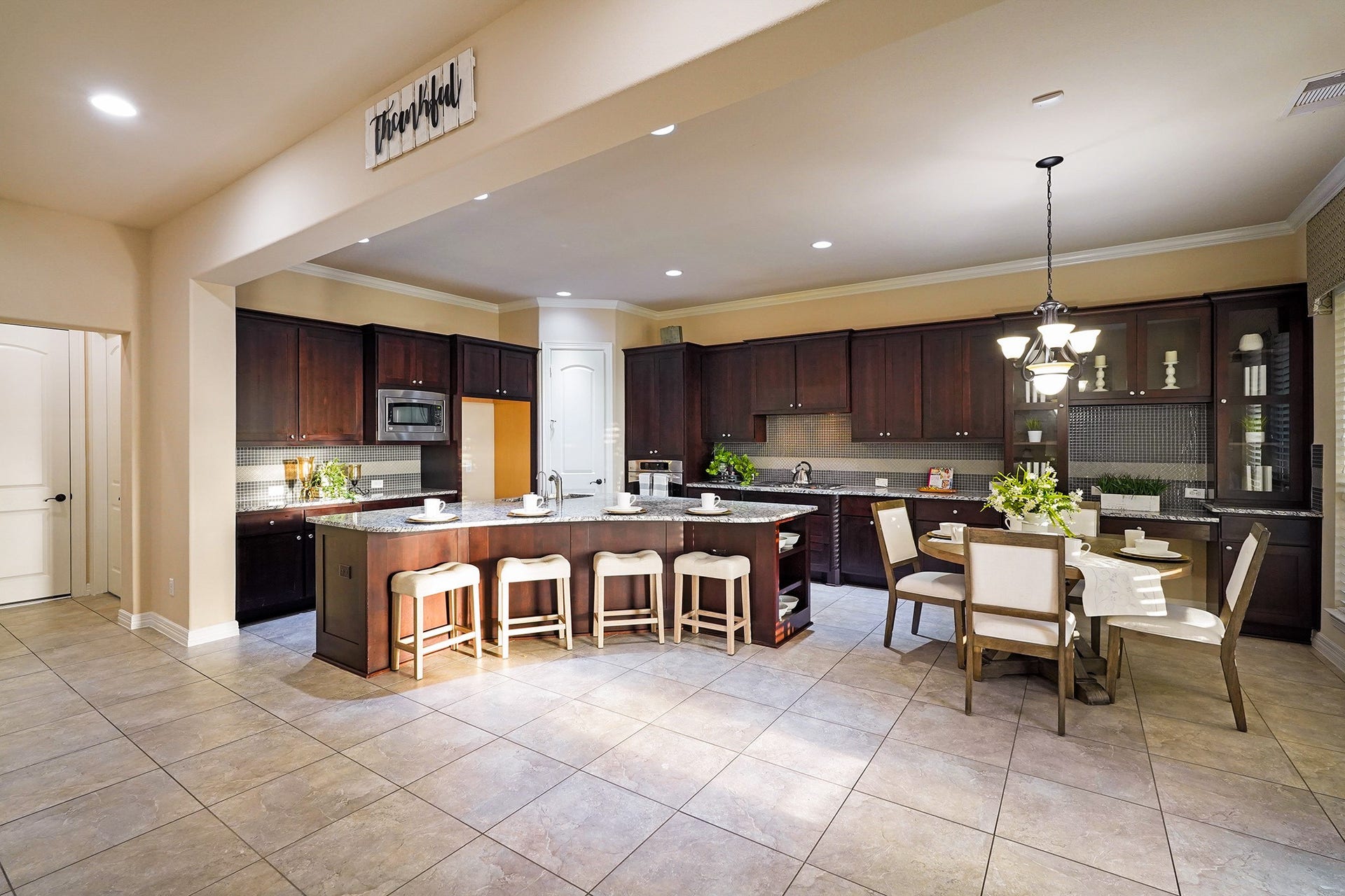 3102 Barrons Way, Sugar Land, TX 77479 The kitchen features dark wood cabinetry, a large island with seating for four, and ample counter space. It's well-lit with recessed lighting and a stylish chandelier over the adjacent dining area, creating a welcoming atmosphere for cooking and entertaining.