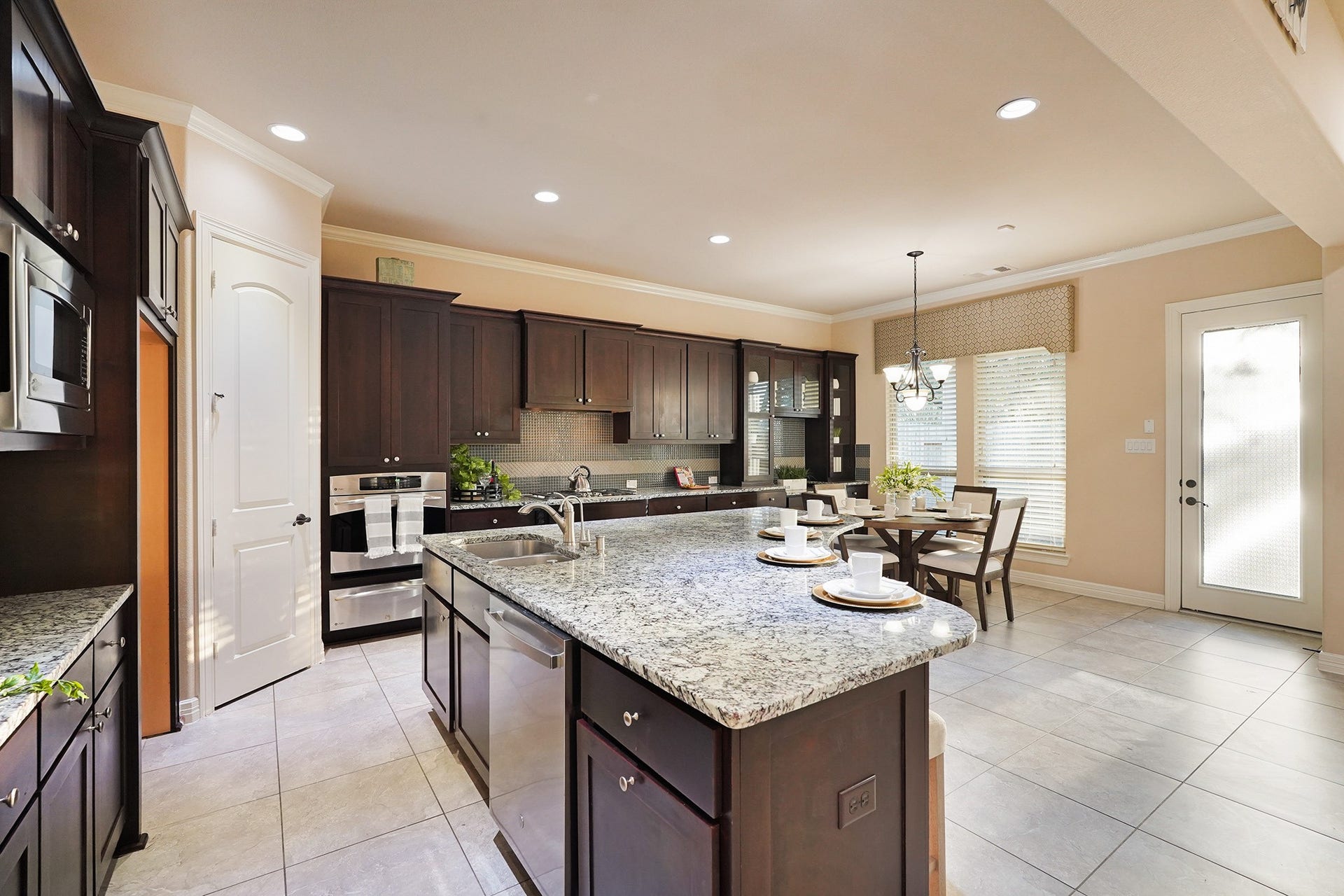 3102 Barrons Way, Sugar Land, TX 77479 This spacious kitchen features dark wood cabinetry, a large granite island with seating, stainless steel appliances, and a bright dining area with natural light from large windows and a glass door.