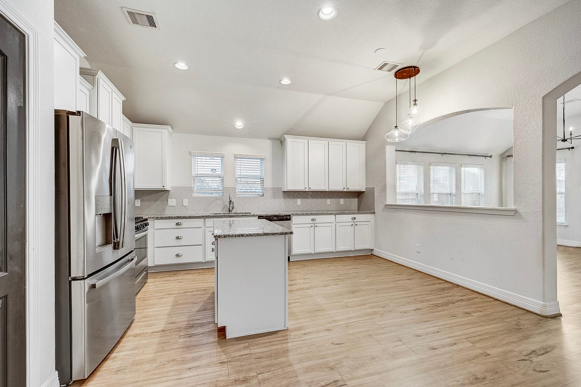 40638 Goldeneye Place, Magnolia, TX 77354 Spacious kitchen featuring modern stainless steel appliances, elegant white cabinetry, and a central island, all set on warm wood flooring and illuminated by stylish pendant lighting.
