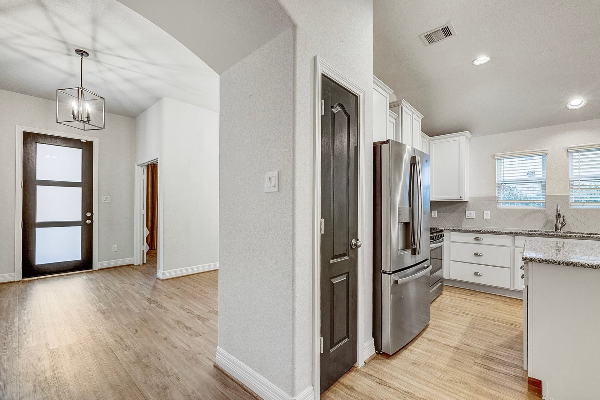 40638 Goldeneye Place, Magnolia, TX 77354 Bright, modern entryway with sleek hardwood flooring leads into a stylish kitchen featuring stainless steel appliances, granite countertops, and ample natural light from dual windows.