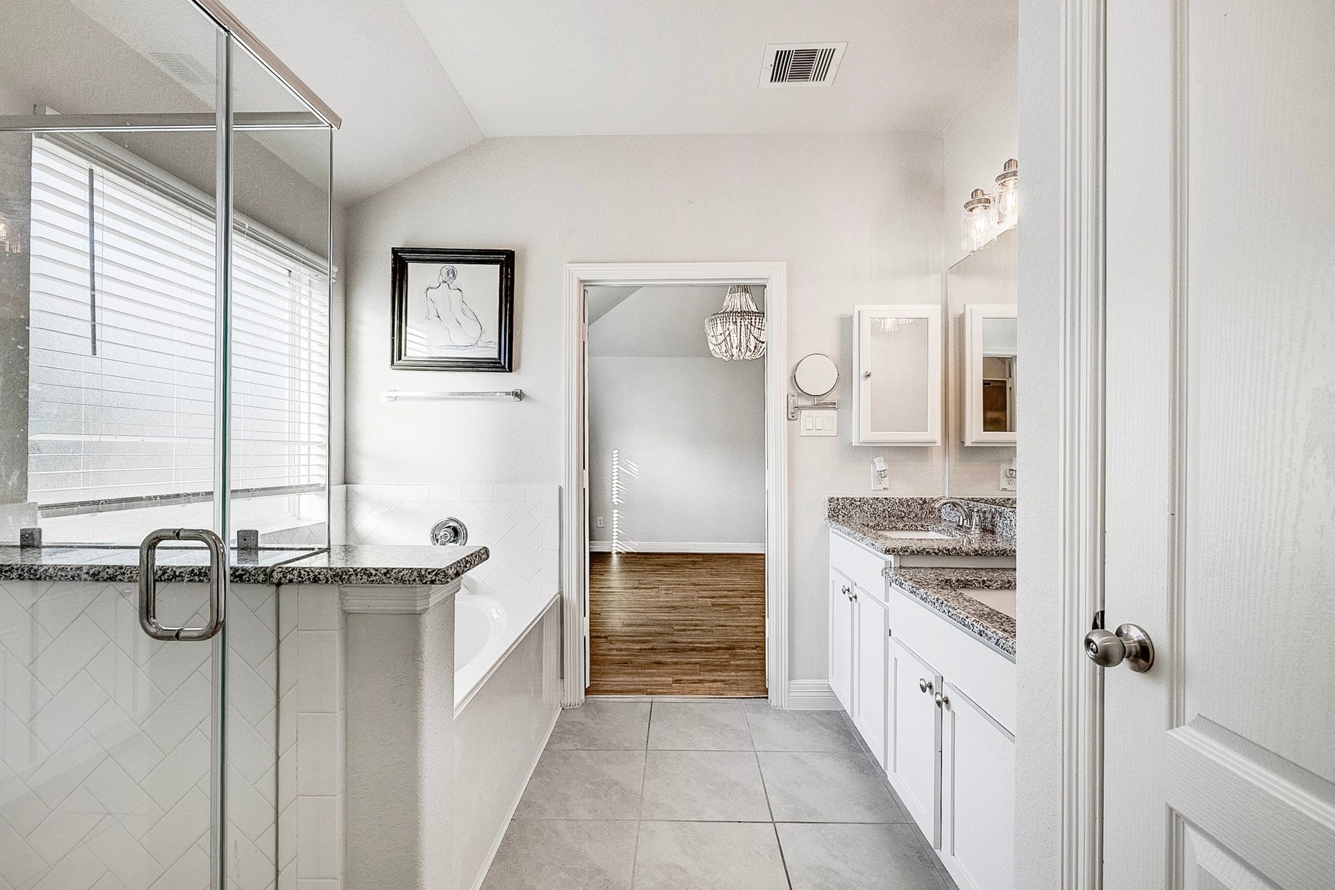 40638 Goldeneye Place, Magnolia, TX 77354 This elegant bathroom features a spacious glass-enclosed shower, a luxurious soaking tub, and dual vanities with granite countertops, leading to a bright room with hardwood flooring.