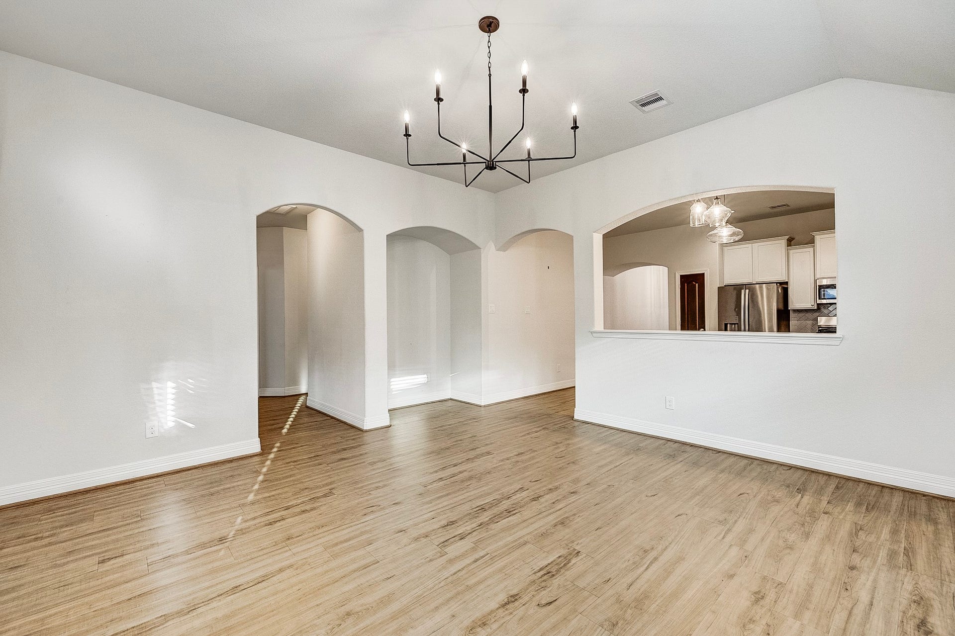 40638 Goldeneye Place, Magnolia, TX 77354 Bright and inviting open-concept space featuring elegant wood flooring, modern light fixtures, and charming arched entryways, seamlessly connecting to the kitchen area.