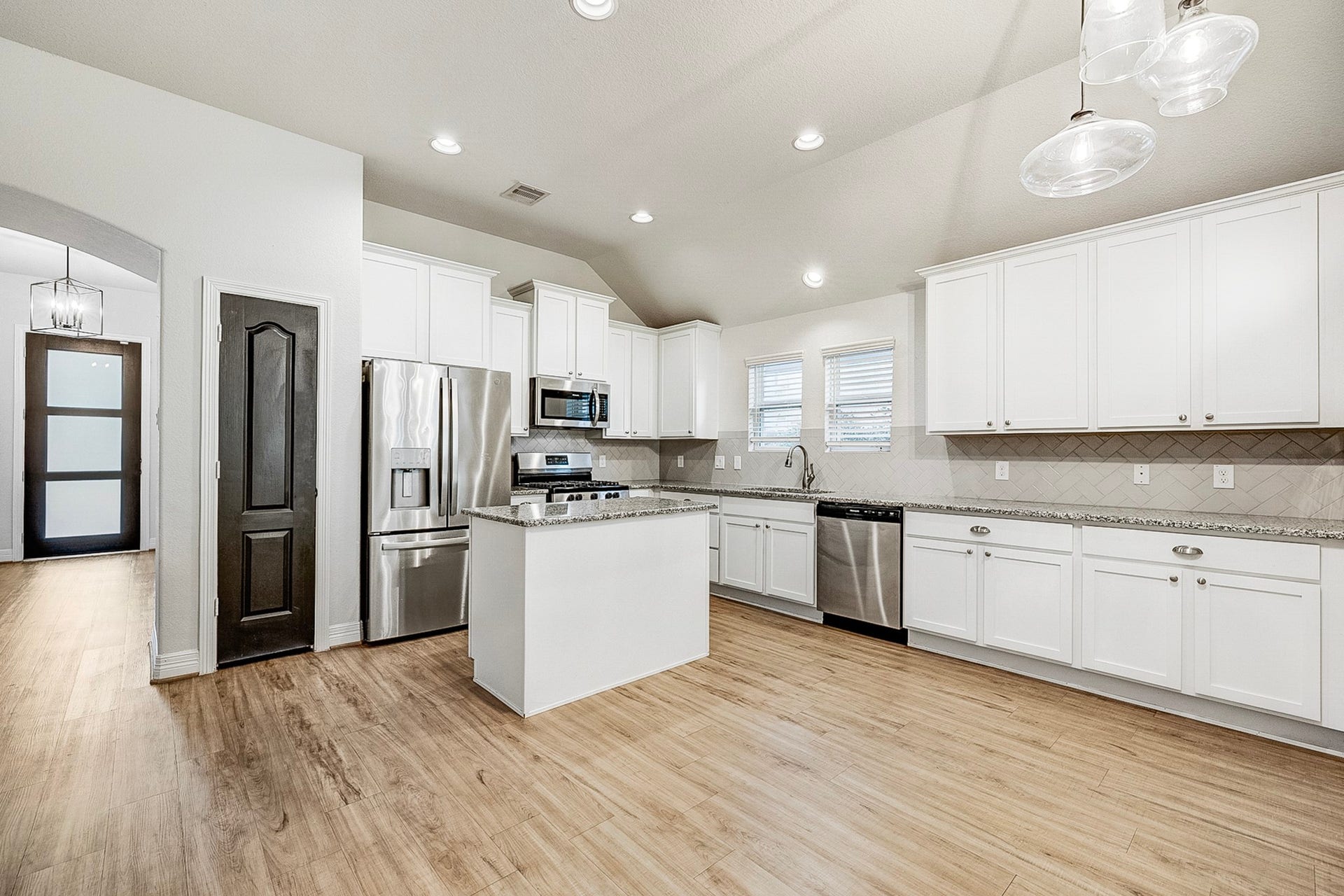 40638 Goldeneye Place, Magnolia, TX 77354 Spacious kitchen featuring sleek stainless steel appliances, pristine white cabinetry, and elegant granite countertops, complemented by warm wood flooring and modern lighting.