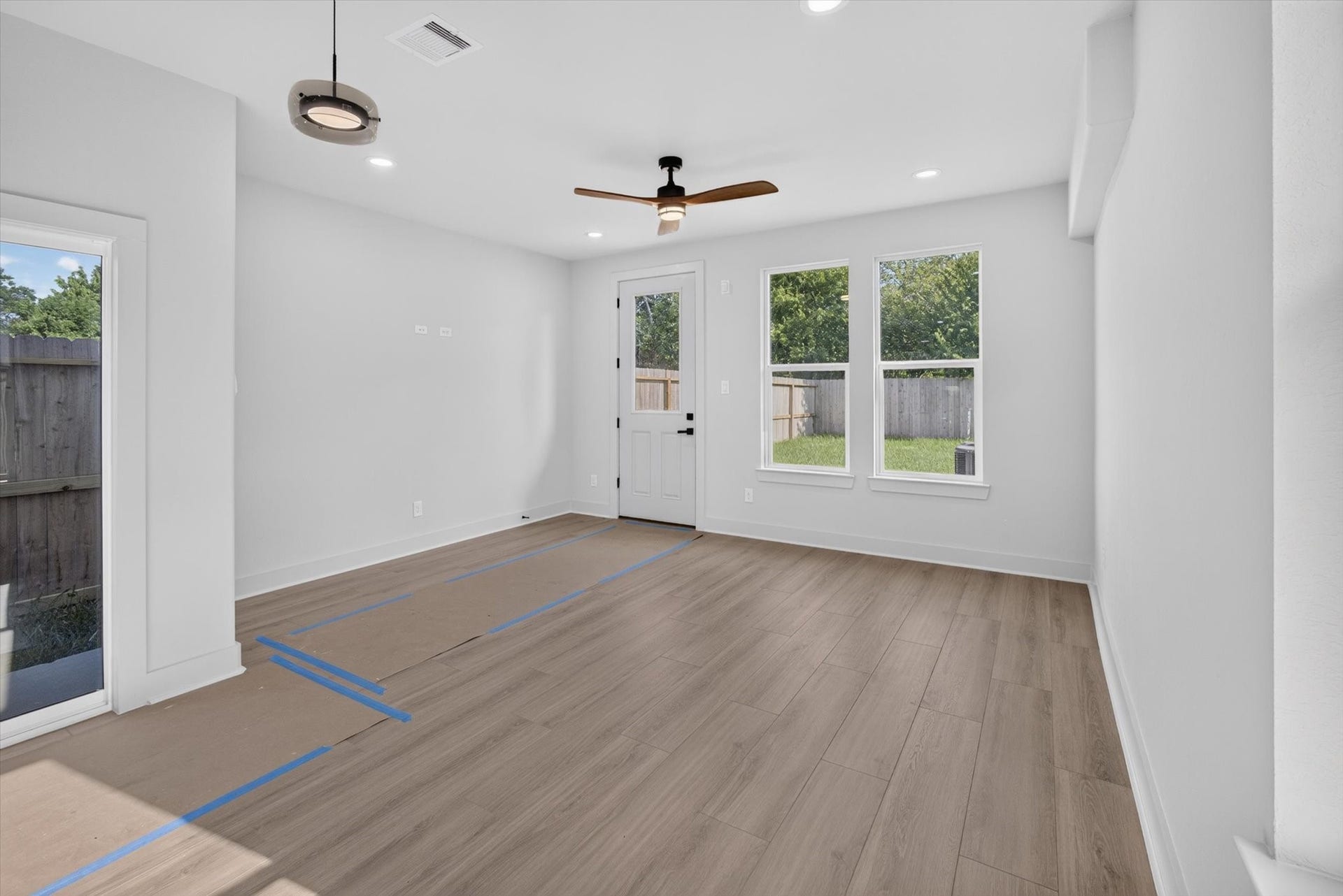 8027 BETTY BOOP Street, Houston, TX 77028 This open-concept kitchen and living area features a sleek island with a marble countertop, modern pendant lighting, and light wood cabinetry. The space is bright and airy with large windows, stylish gray walls, and wood-look flooring, providing a contemporary and inviting atmosphere.