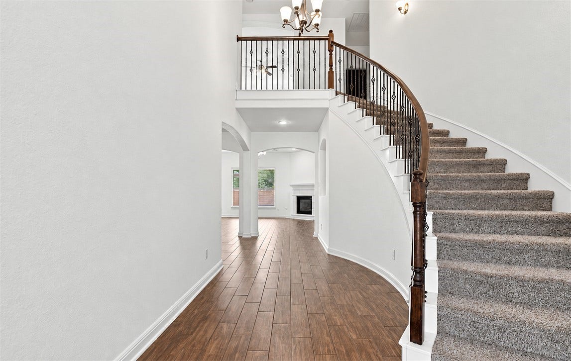 23827 Padauk Tree Trail, Katy, TX 77493 Step inside to a grand two-story entryway with a sweeping curved staircase, wrought iron railing, hardwood floors, and a chandelier that makes every entrance feel special.