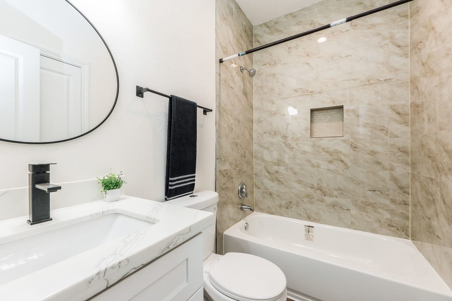 Elegant bathroom featuring a sleek vanity with a marble countertop, an oval mirror, and a chic shower-tub combination with stylish tile work.
