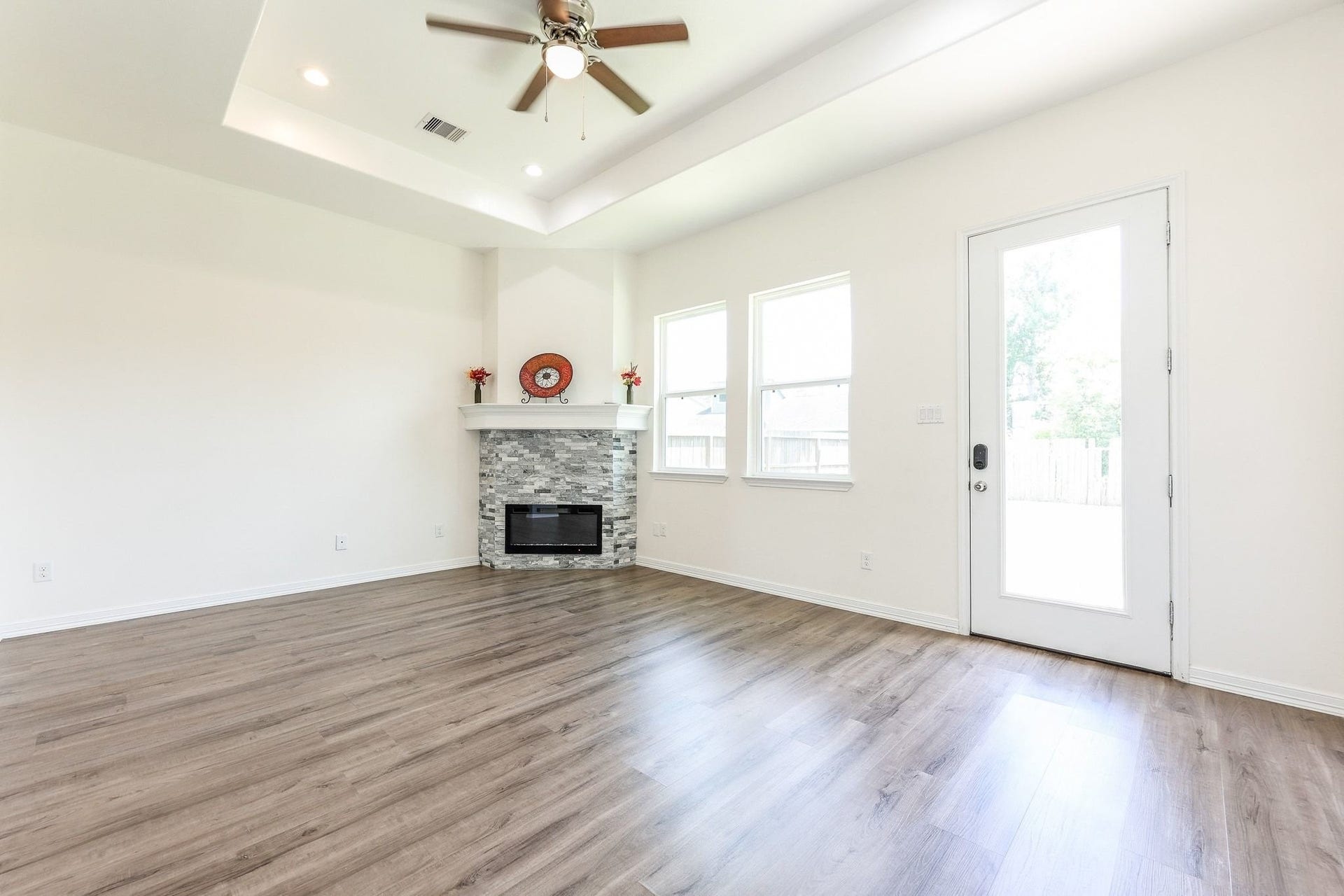 Bright and airy living space with a modern stone fireplace, high ceilings, and elegant wood flooring, perfect for relaxation and entertaining.