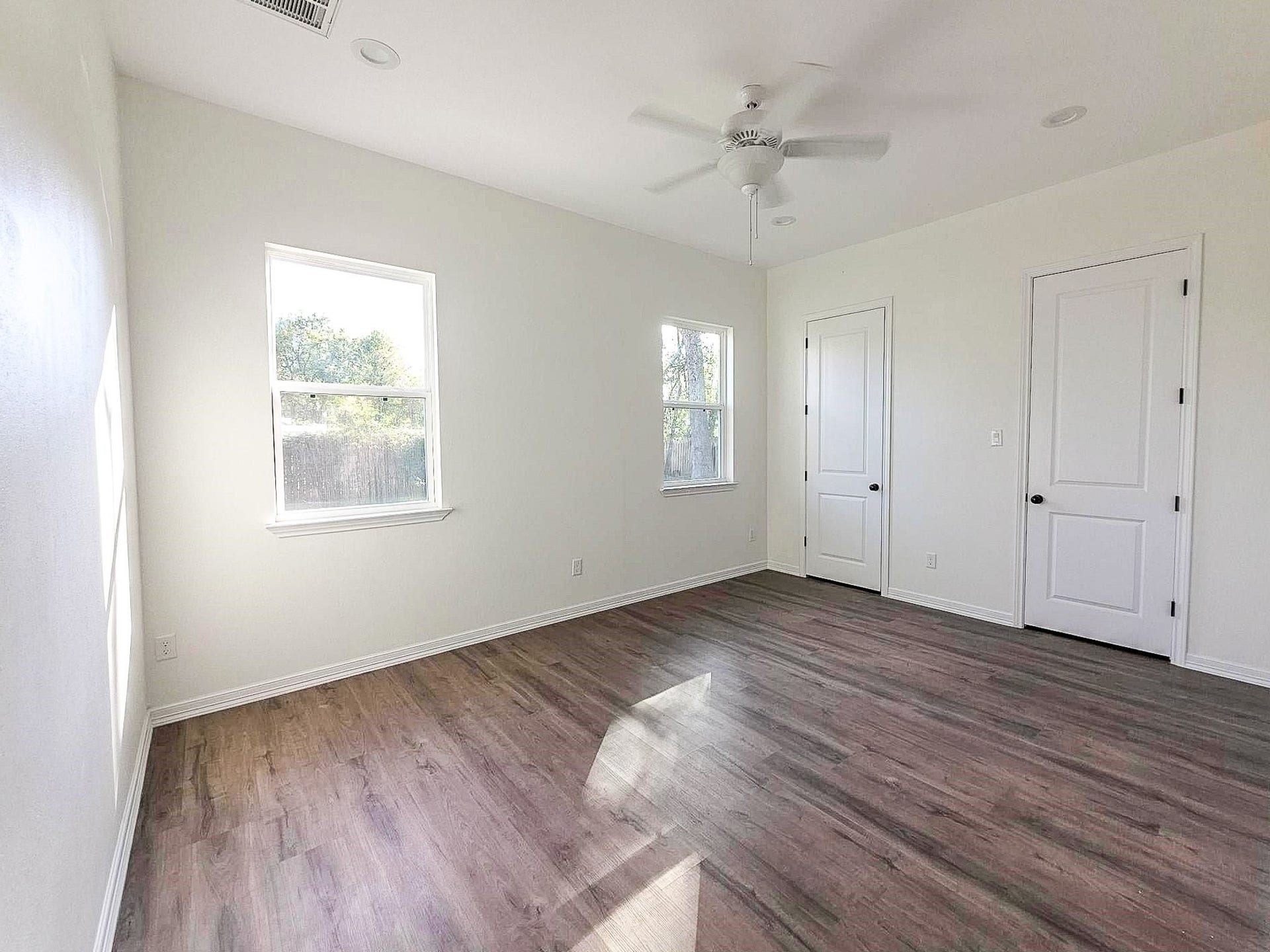 Bright, airy room featuring large windows, sleek wood flooring, and a ceiling fan, offering a comfortable and inviting space.