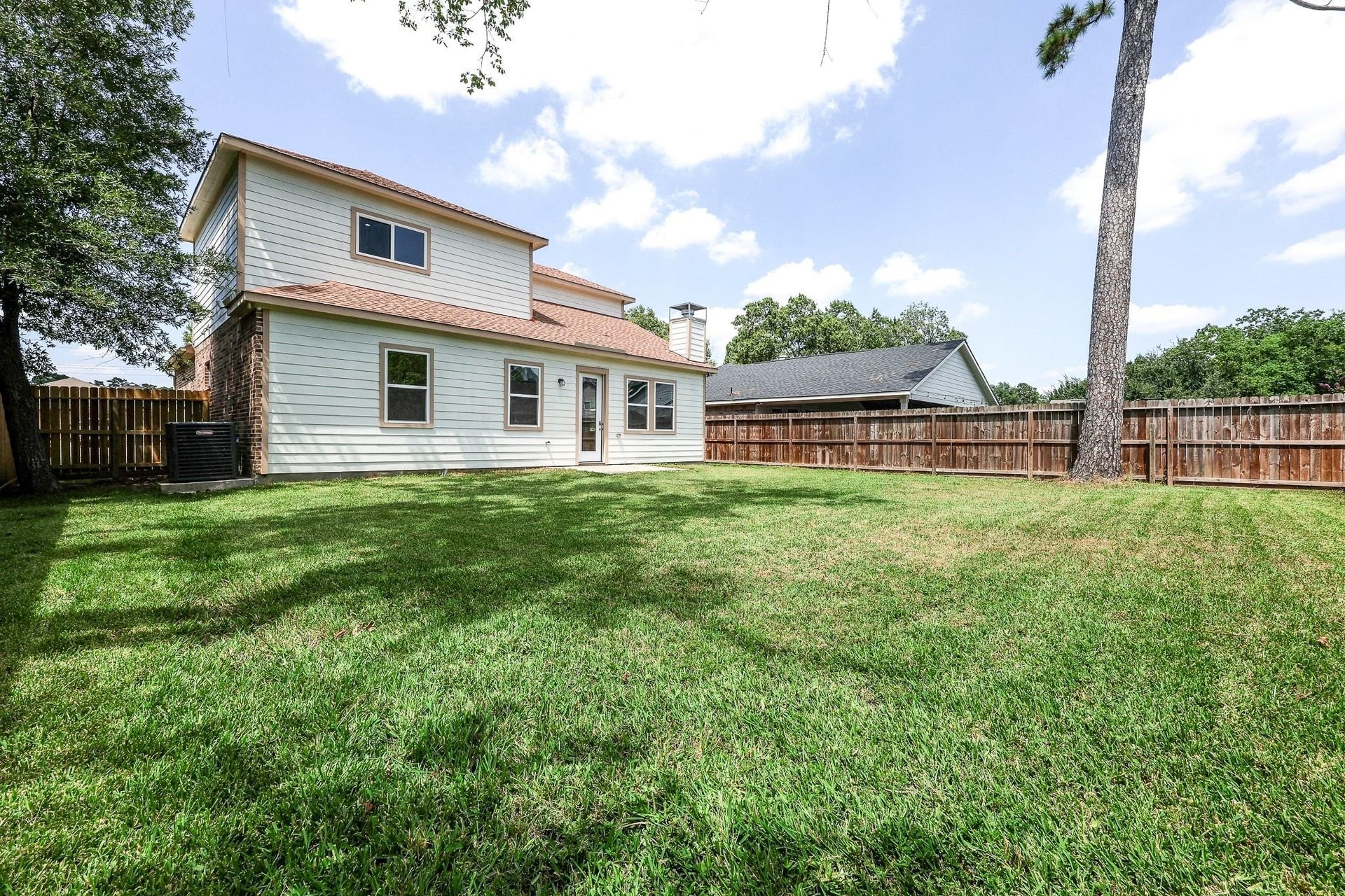 Spacious backyard with lush green lawn, perfect for outdoor activities, featuring a well-maintained two-story home and a privacy fence.