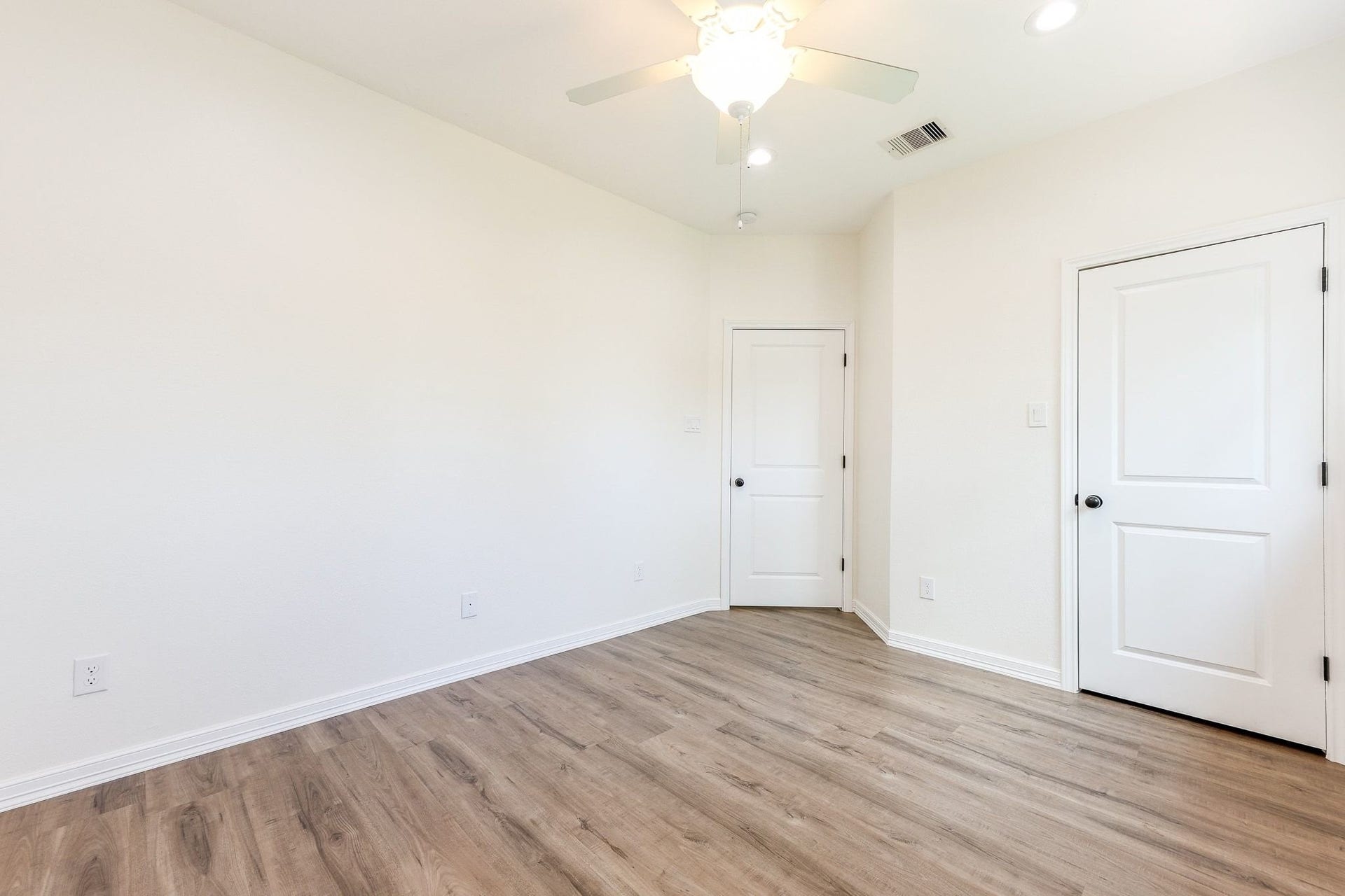 Bright room with sleek Laminated flooring, two white doors, and a ceiling fan, offering a versatile space for any purpose.