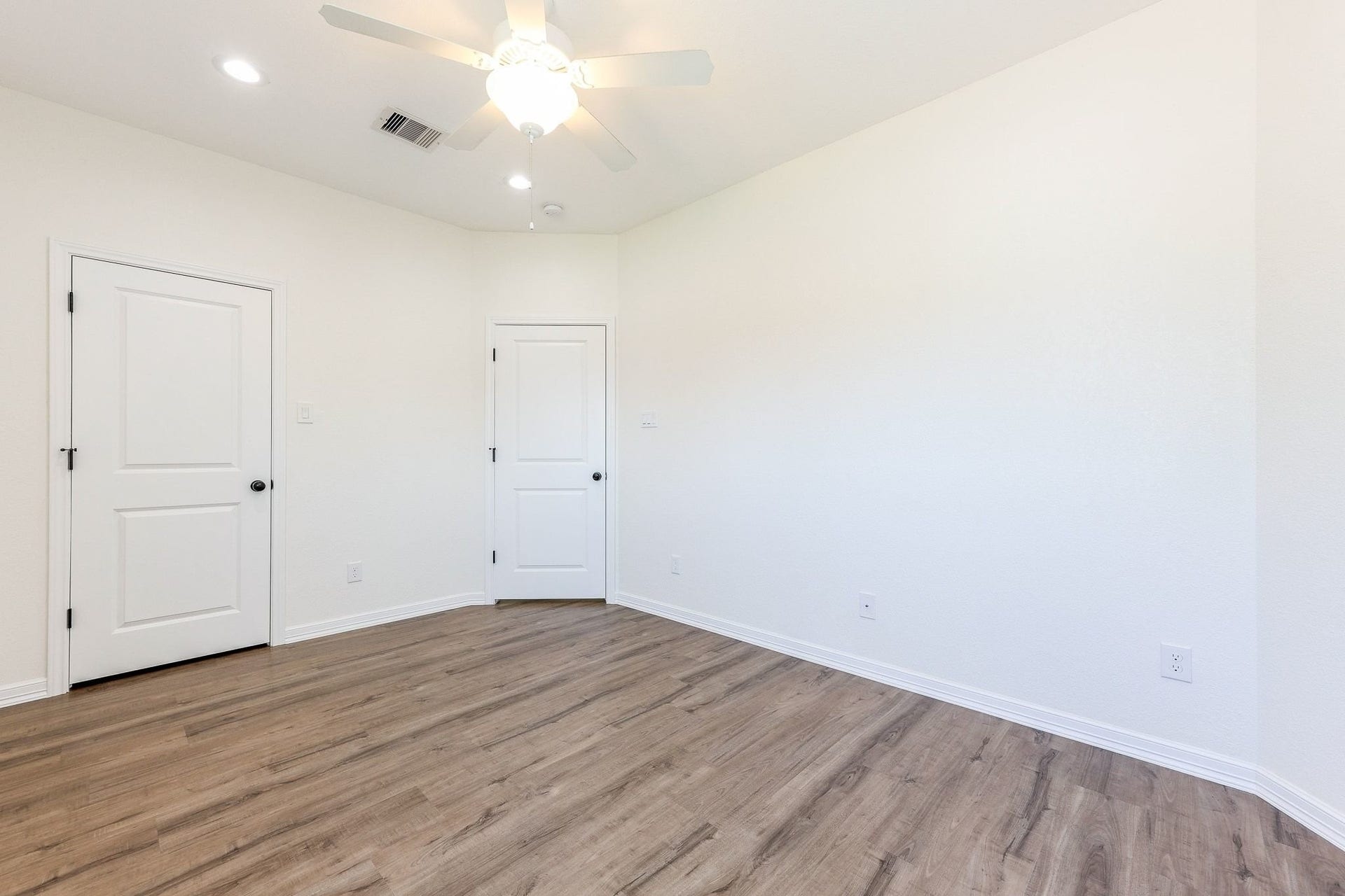 Bright, spacious room with modern Laminated flooring and soft white walls, featuring a ceiling fan for comfort and dual doors for versatile use.