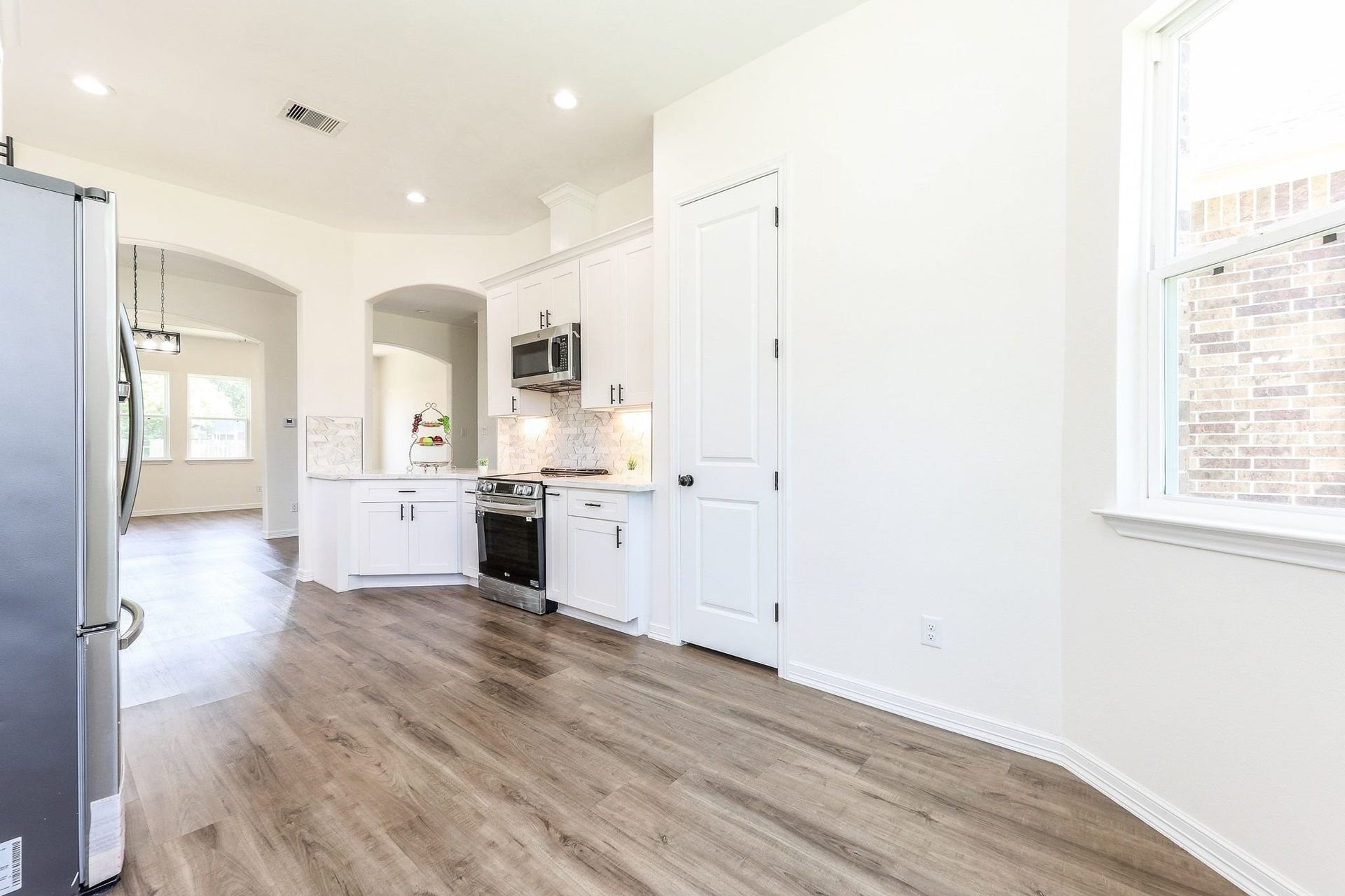 Bright and airy kitchen featuring modern stainless steel appliances, sleek white cabinetry, and elegant wood flooring, seamlessly flowing into an open dining area with abundant natural light.