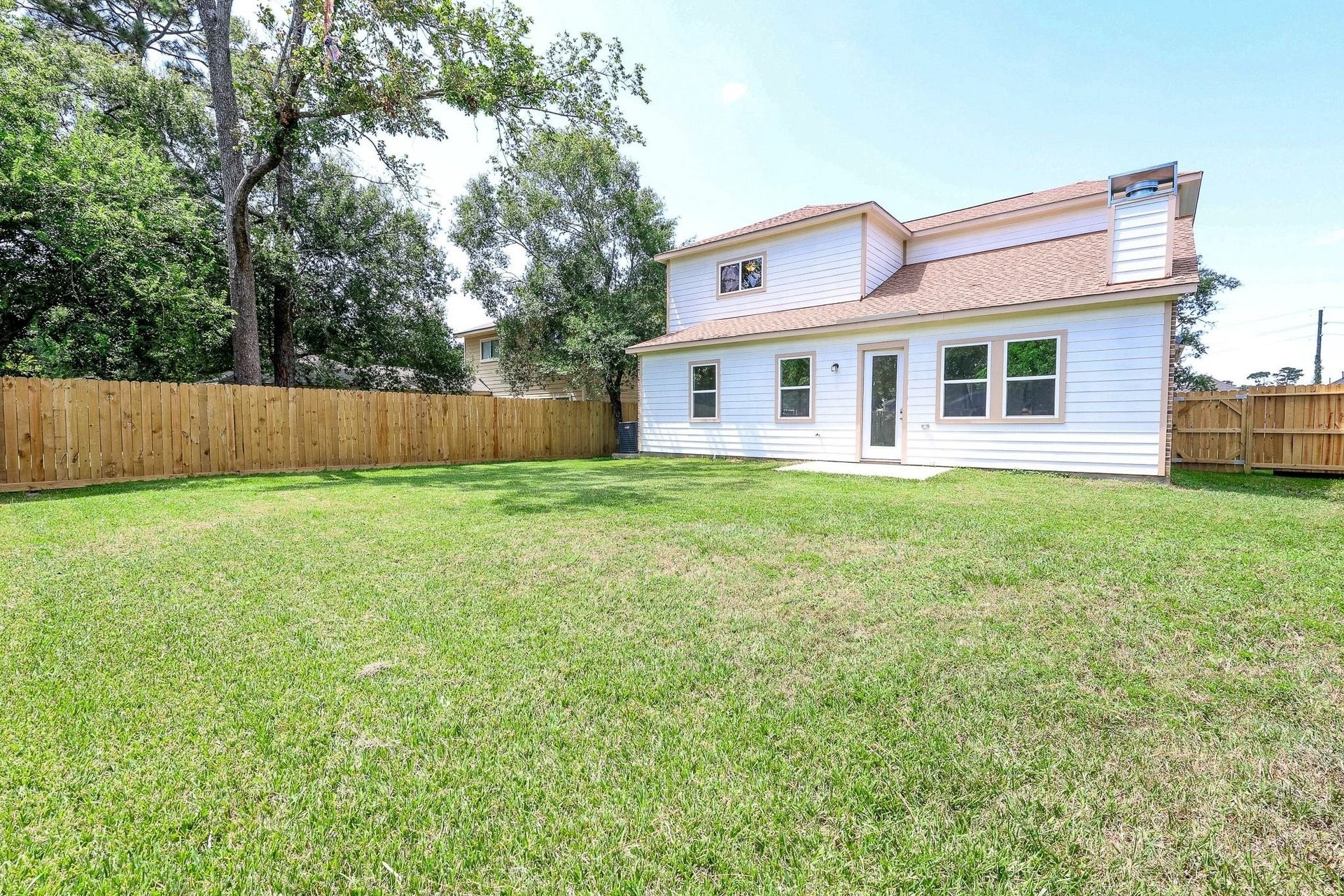 Spacious backyard with lush grass and privacy fence, perfect for outdoor activities and relaxation, complemented by a charming two-story home with large windows and a patio door.