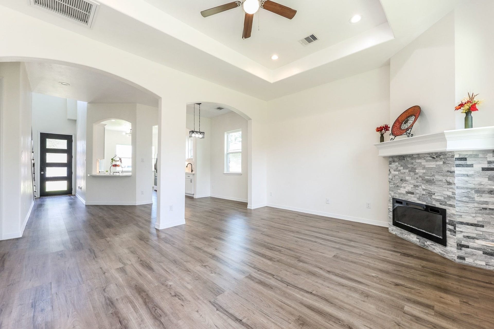 Spacious living area features elegant laminated flooring, a modern stone fireplace, and high ceilings with recessed lighting, creating a bright and inviting atmosphere.