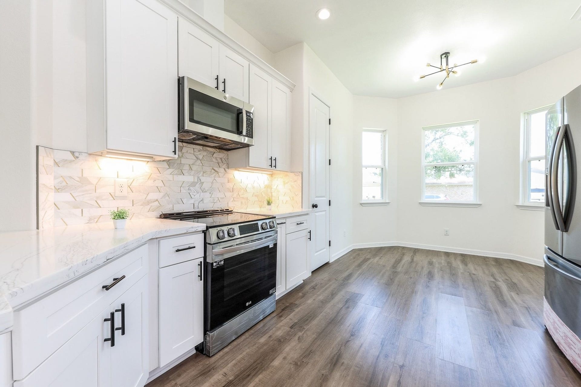 Bright and modern kitchen featuring sleek white cabinetry, stainless steel appliances, and elegant marble countertops, complemented by a spacious breakfast nook with large windows.