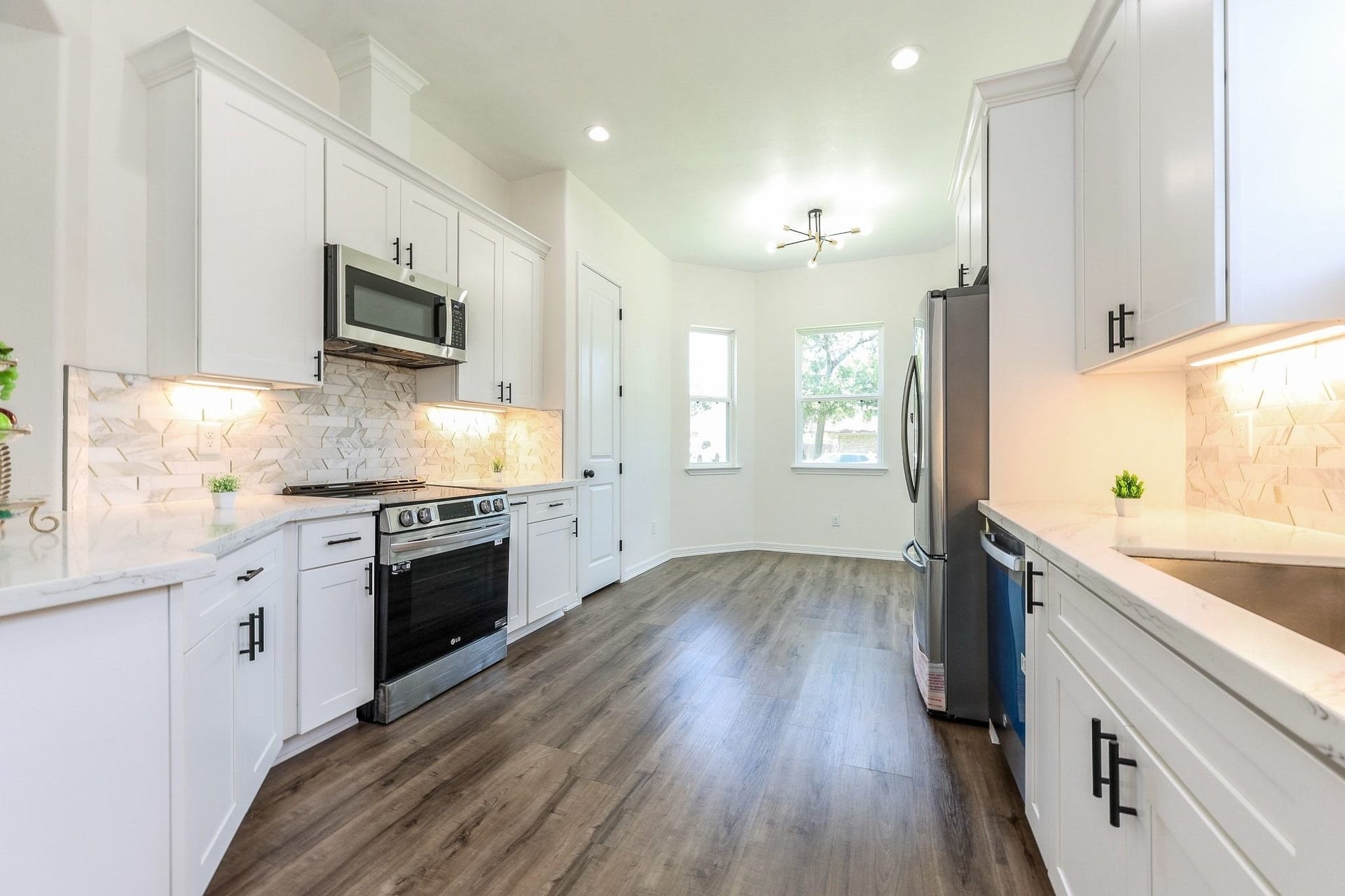Sleek modern kitchen featuring white cabinetry, stainless steel appliances, and elegant marble countertops with a stylish tile backsplash.