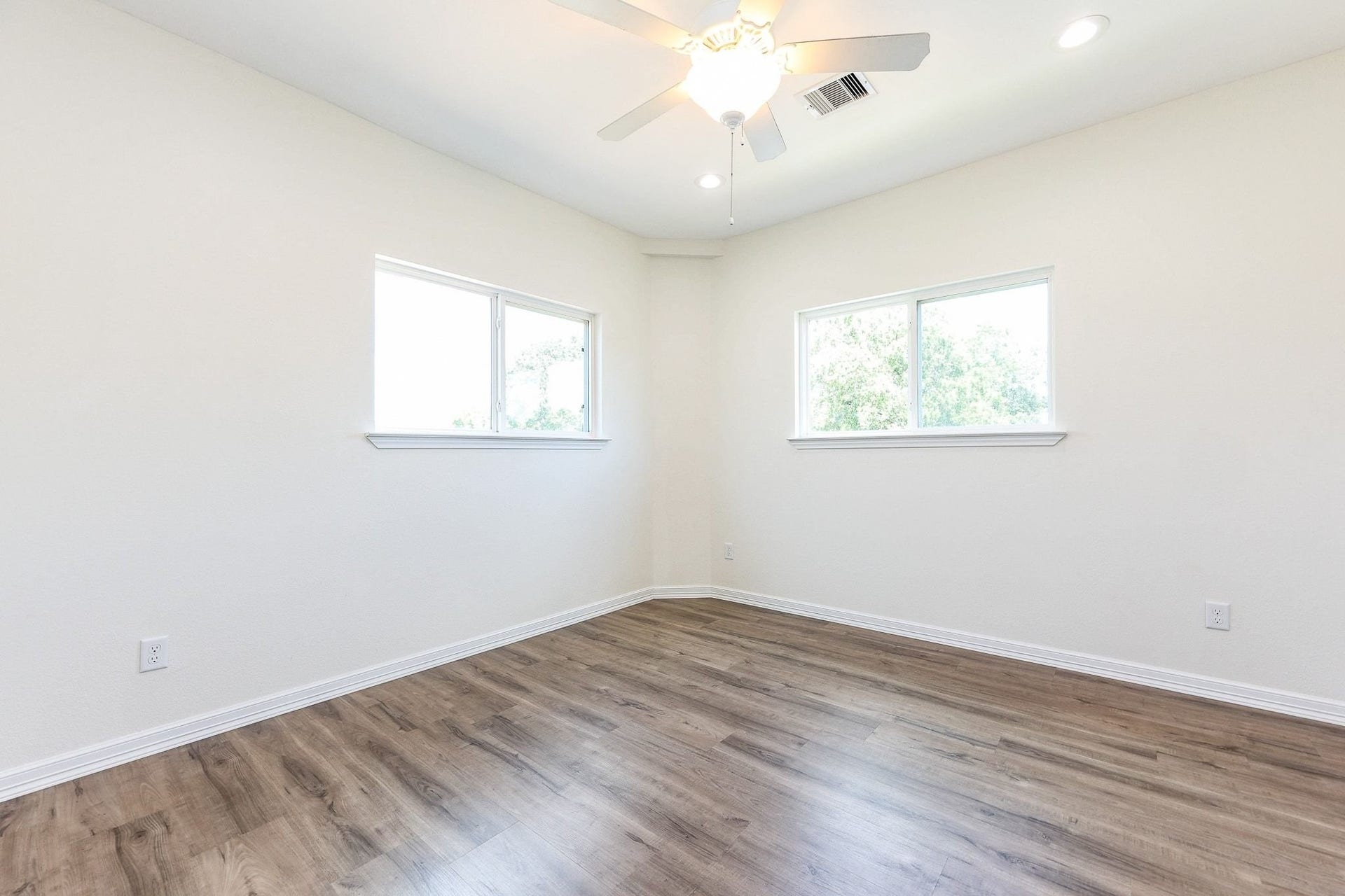Bright and airy room featuring sleek laminate flooring, neutral walls, and dual windows for abundant natural light, complete with a ceiling fan for comfort.