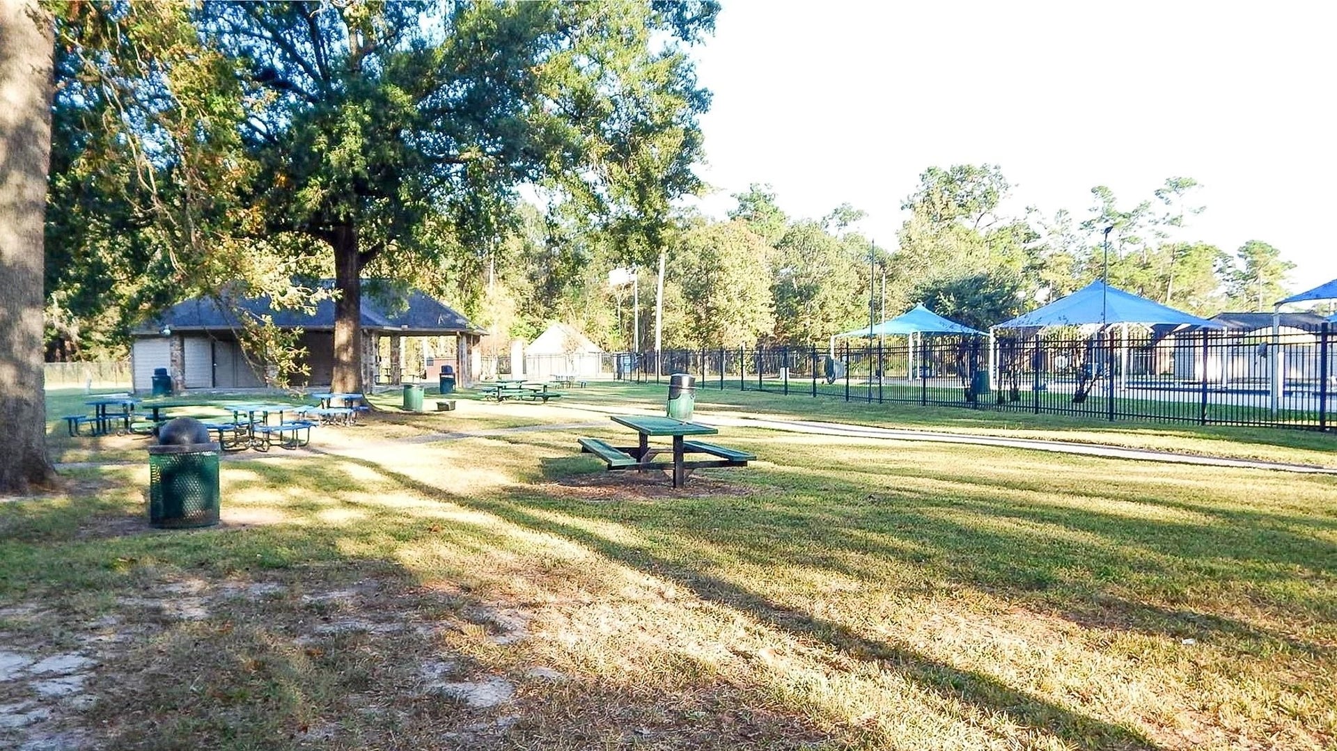 Spacious park setting with shaded picnic areas, mature trees, and nearby pool facilities, perfect for outdoor gatherings and relaxation.