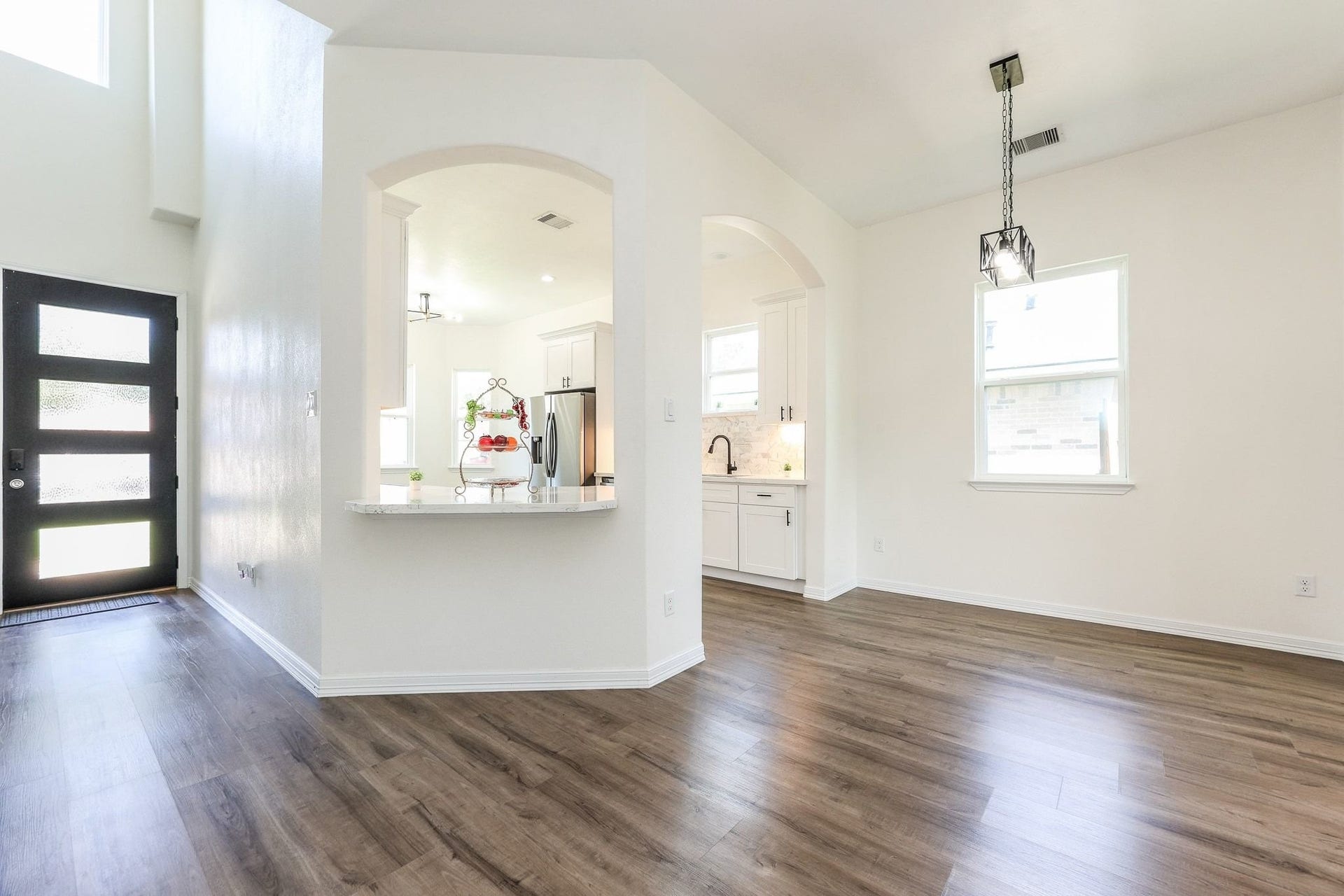 Bright and spacious open-plan living area featuring elegant laminated flooring, a modern kitchen with white cabinetry, and a stylish front door that enhances the contemporary feel.