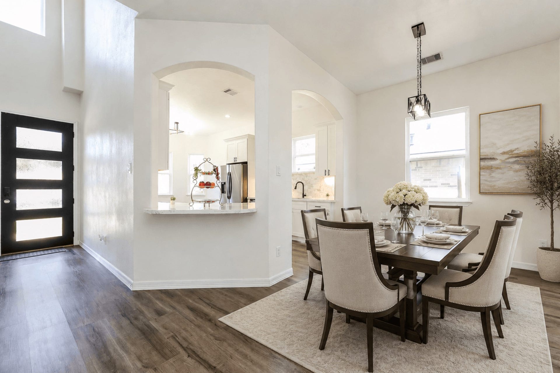 Bright and inviting dining area featuring elegant seating, a chic light fixture, and a view into a modern kitchen, all complemented by sleek flooring and a stylish front entry.
Stage Dining
