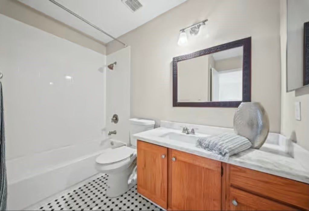 2555 Bering Drive, #1, Houston, TX 77057 Charming 2nd bathroom featuring a classic black-and-white tile floor, a spacious vanity with wood cabinetry, and a modern mirror. The shower-tub combo adds functionality and style. An addition half bathroom is located downstairs in the hallway