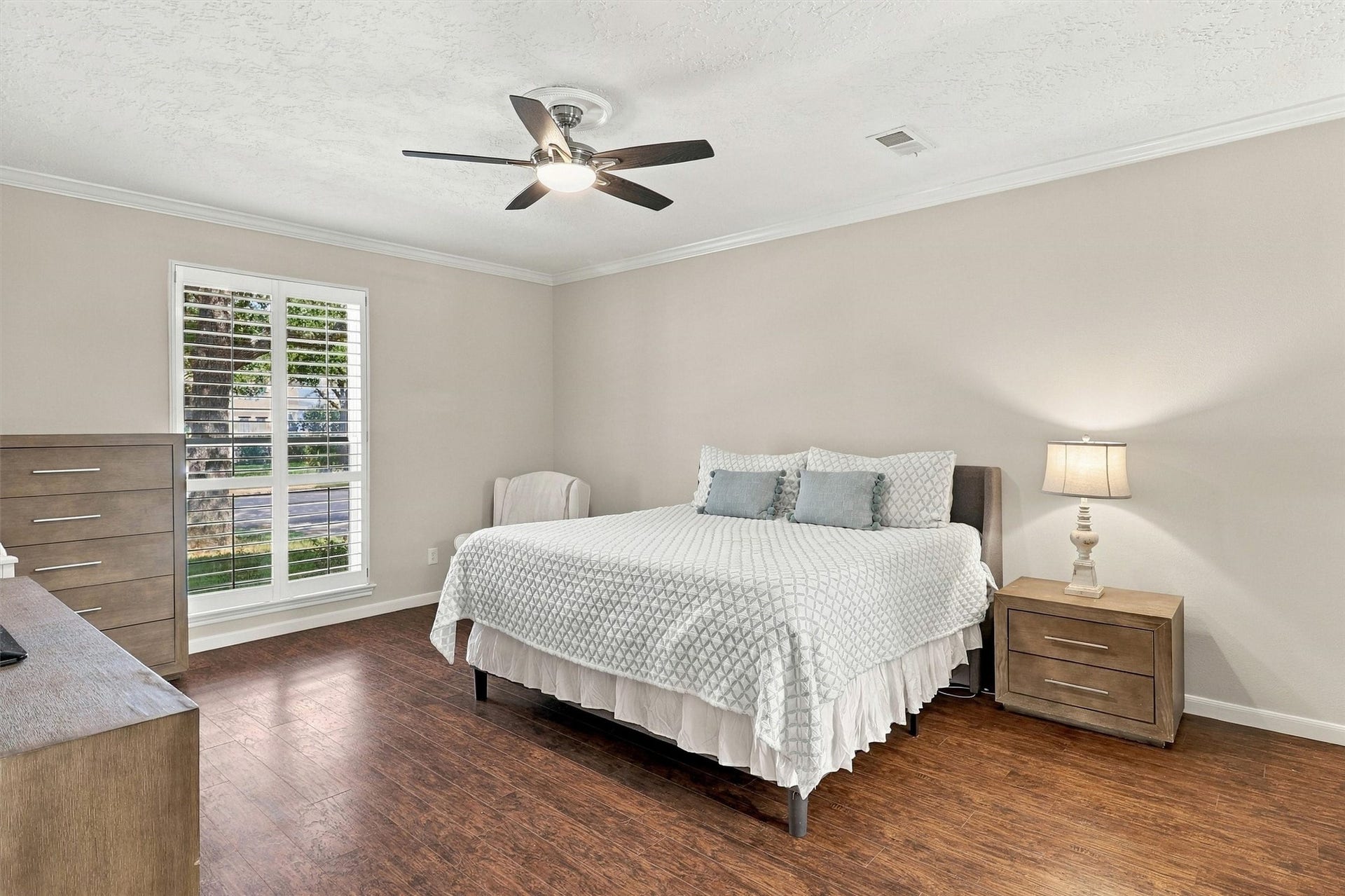 1030 Barkston Drive, Katy, TX 77450 The primary bedroom offers a spacious retreat with hardwood floors, designer paint, elegant crown molding, and a ceiling fan, along with a large window dressed in plantation shutters that brings in beautiful natural light.