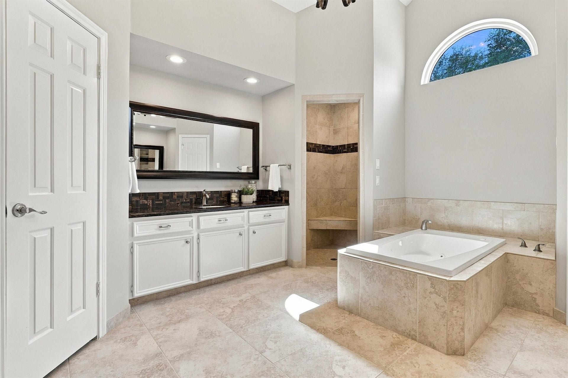 1030 Barkston Drive, Katy, TX 77450 This stunning primary bathroom also features a walk in shower with a neutral tile surround that flows seamlessly with the flooring and tub surround. The arched window above the tub adds a beautiful eye catching detail to the space.