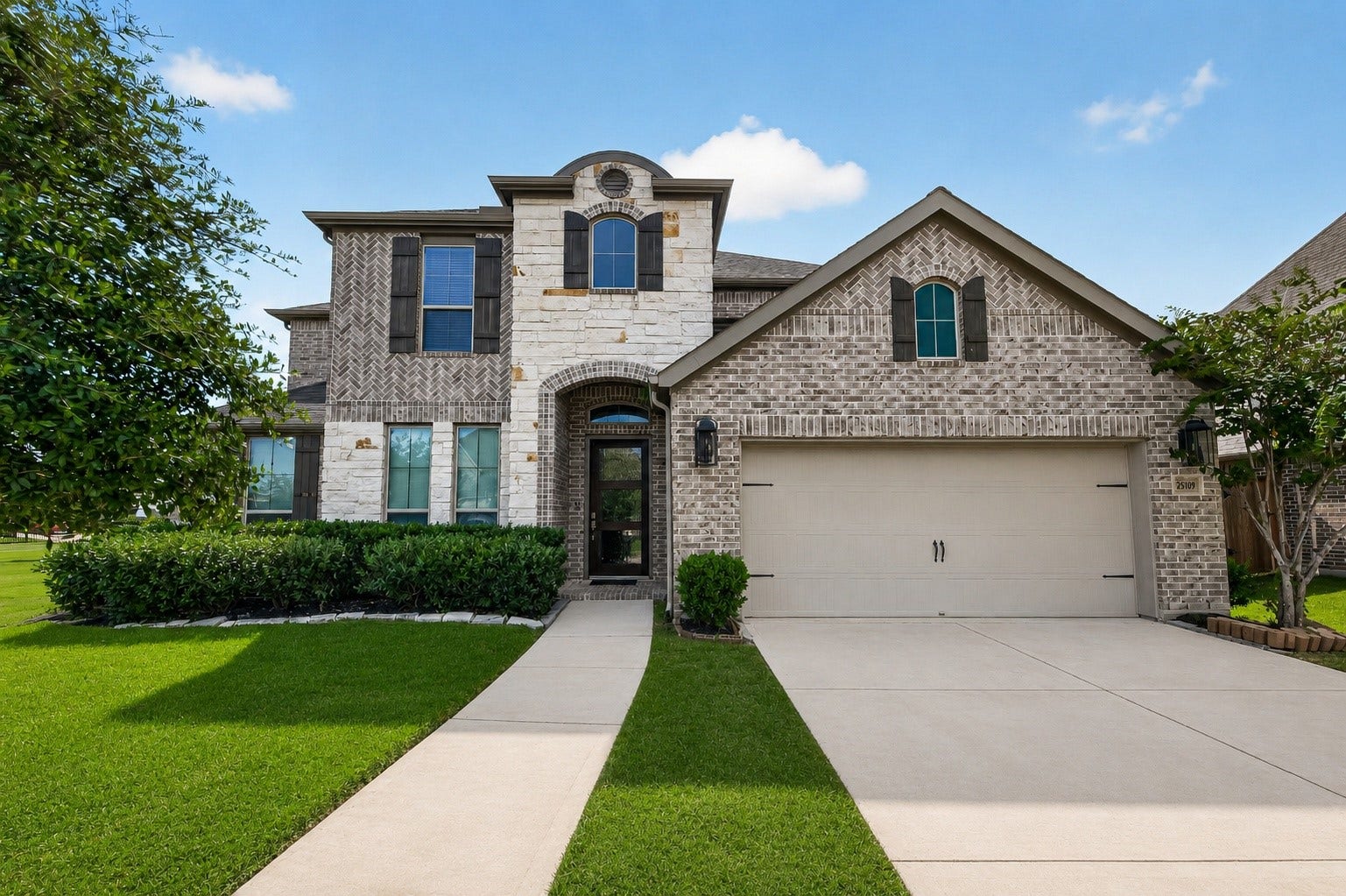 25109 Pinebrook Grove Lane, Tomball, TX 77375 Beautiful two-story home featuring a brick and stone exterior, manicured front lawn, covered entry, and attached garage.