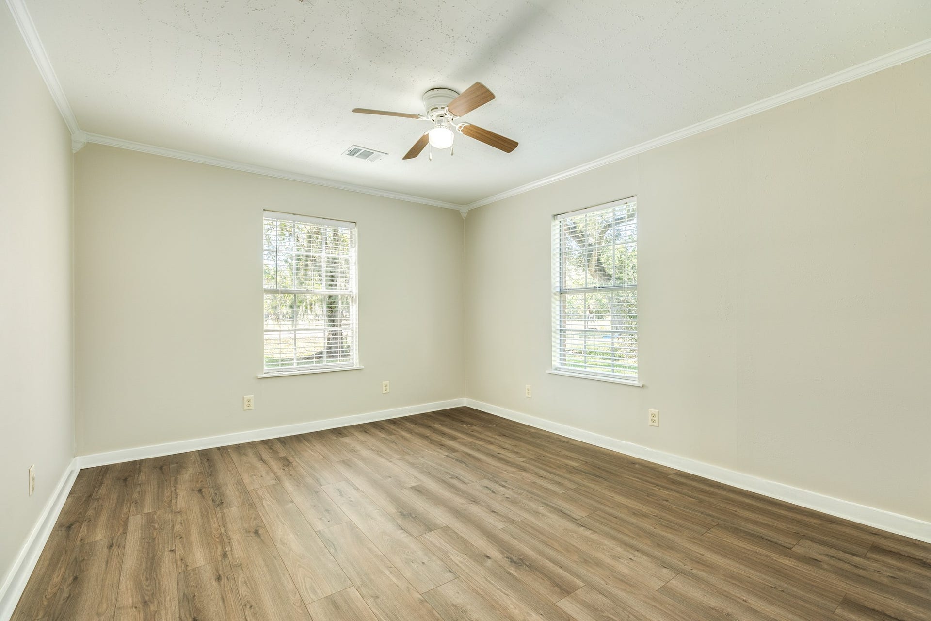 1602 County Road 939, Sweeny, TX 77480 Bright, versatile bedroom showcases attractive wood-look flooring, neutral walls, white trim, and a ceiling fan. Two windows provide natural light and views of the outdoors.