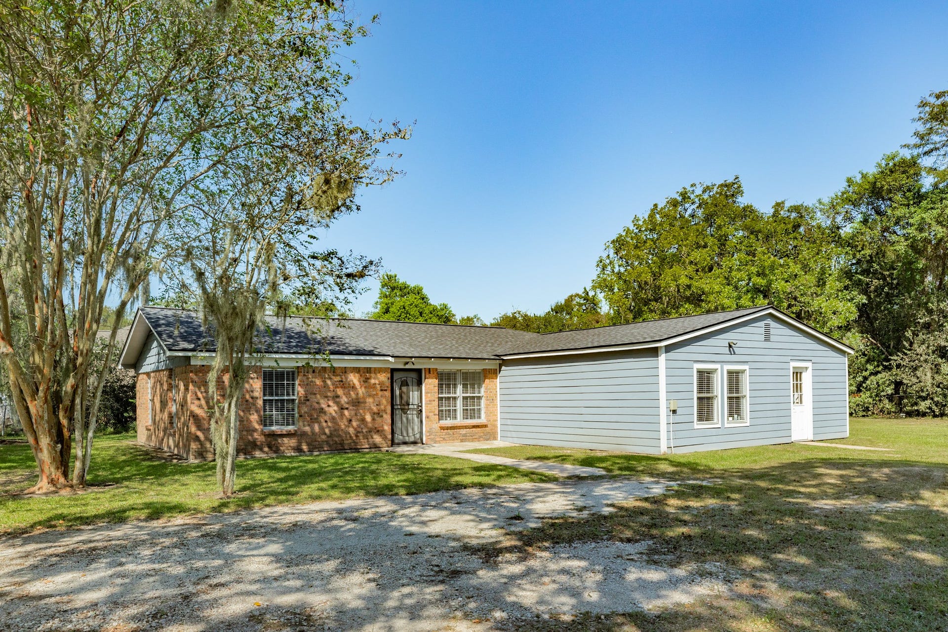 1602 County Road 939, Sweeny, TX 77480 Attractive exterior showcases classic brickwork complemented by blue-gray horizontal siding, white trim, and a dark shingle roof. Mature trees and an open lawn create a peaceful, inviting setting.