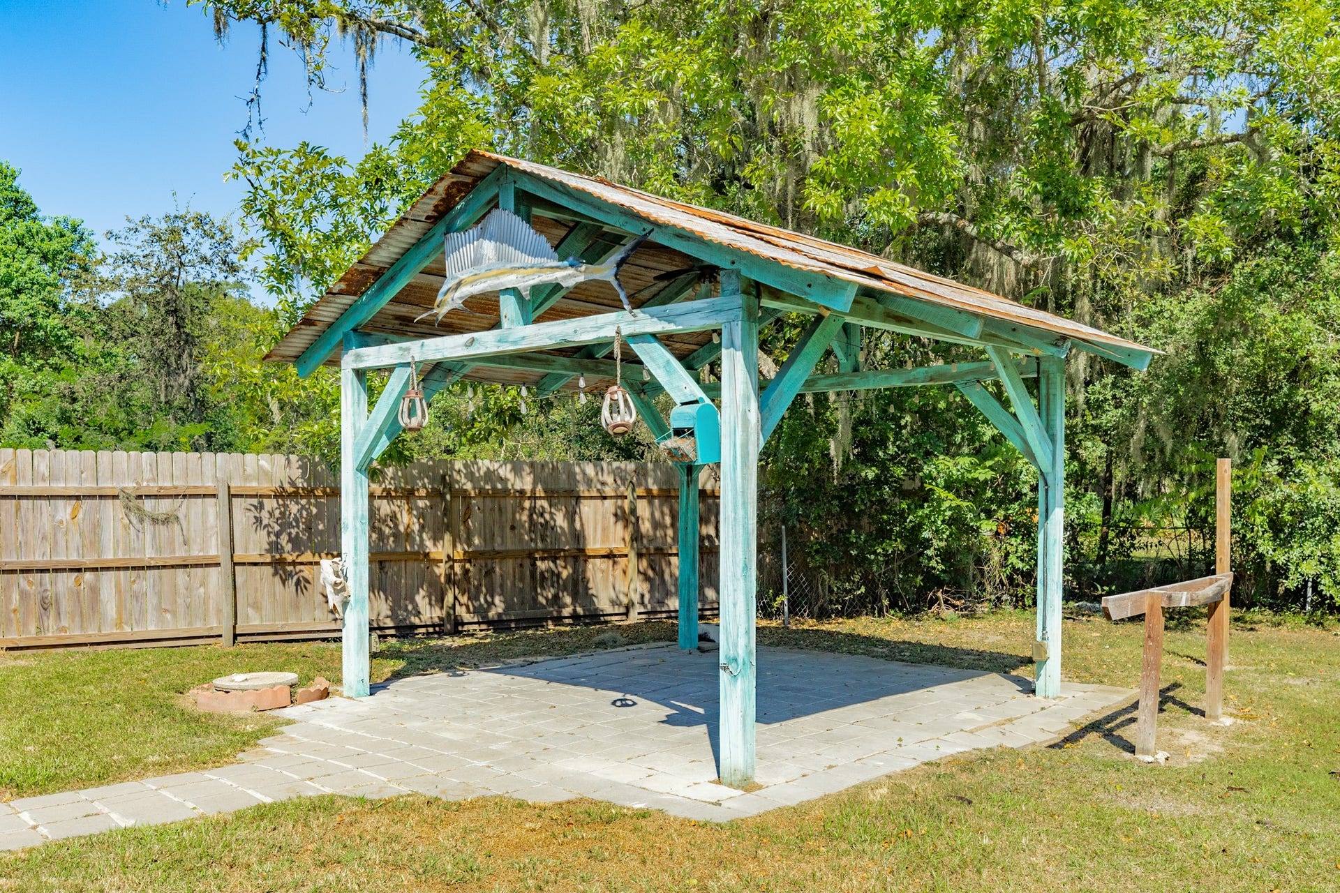 1602 County Road 939, Sweeny, TX 77480 Rustic open-air pavilion features turquoise-painted wooden beams, a metal roof, hanging light fixtures, and a paved foundation. A distinctive outdoor space with room for seating and entertaining.