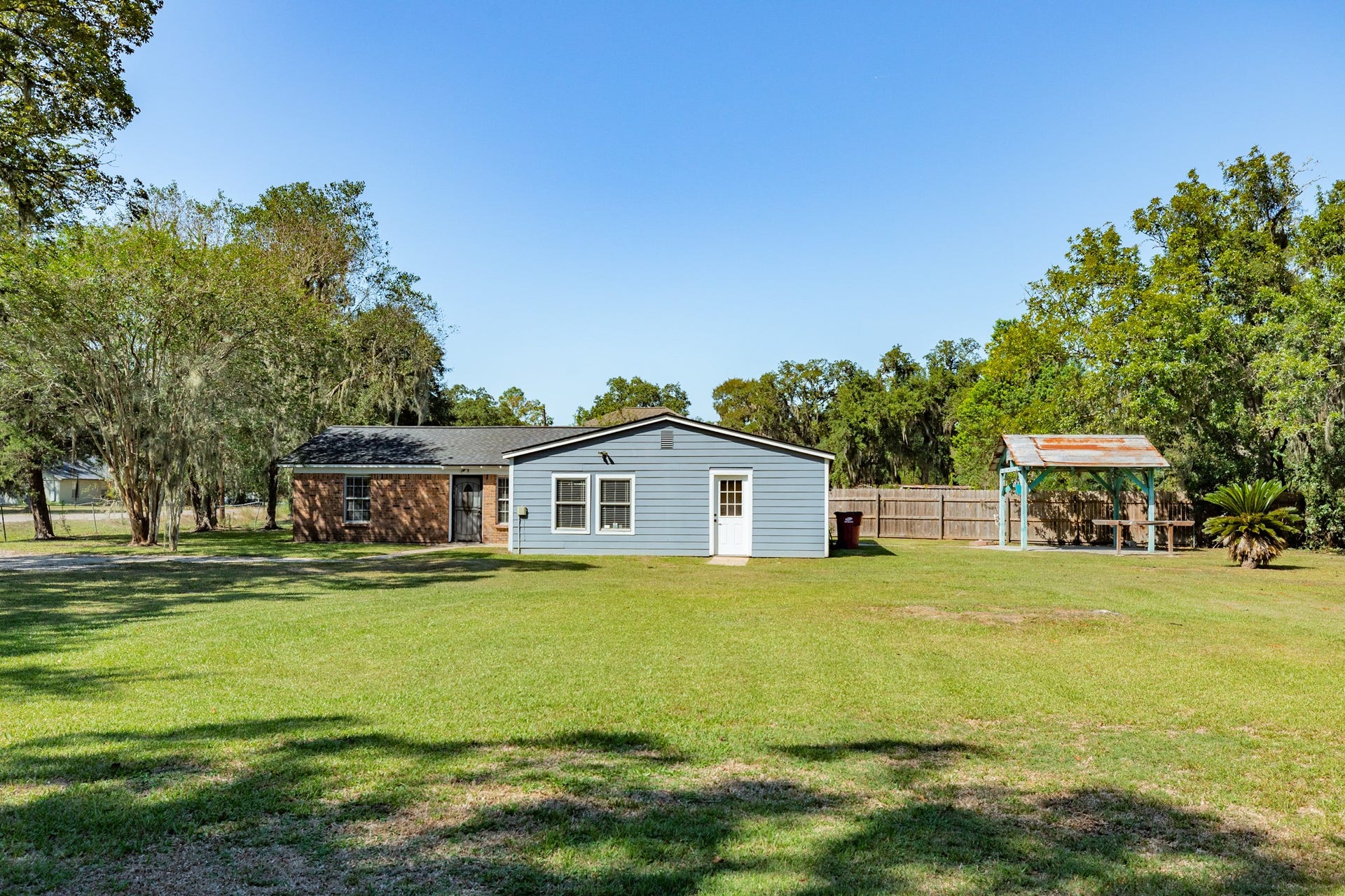 1602 County Road 939, Sweeny, TX 77480 Wide-angle view highlights the home's generous lawn space, mature trees, and open surroundings. A covered outdoor pavilion adds versatility for relaxing or entertaining.