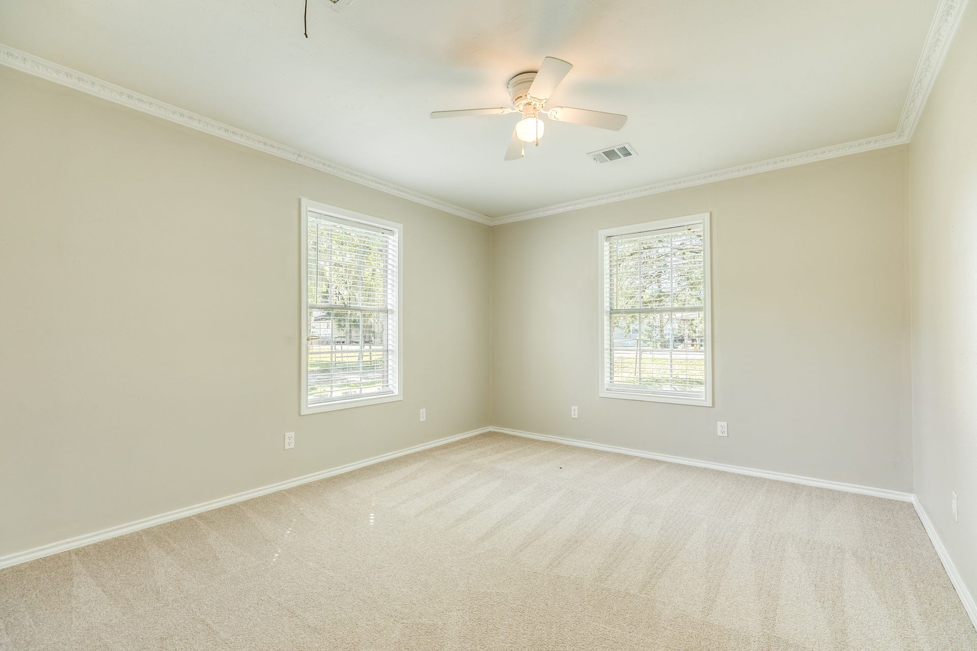 1602 County Road 939, Sweeny, TX 77480 Comfortable bedroom features plush neutral carpeting, decorative crown molding, and a ceiling fan with lighting. Two windows welcome natural light and offer pleasant views of the surrounding greenery.