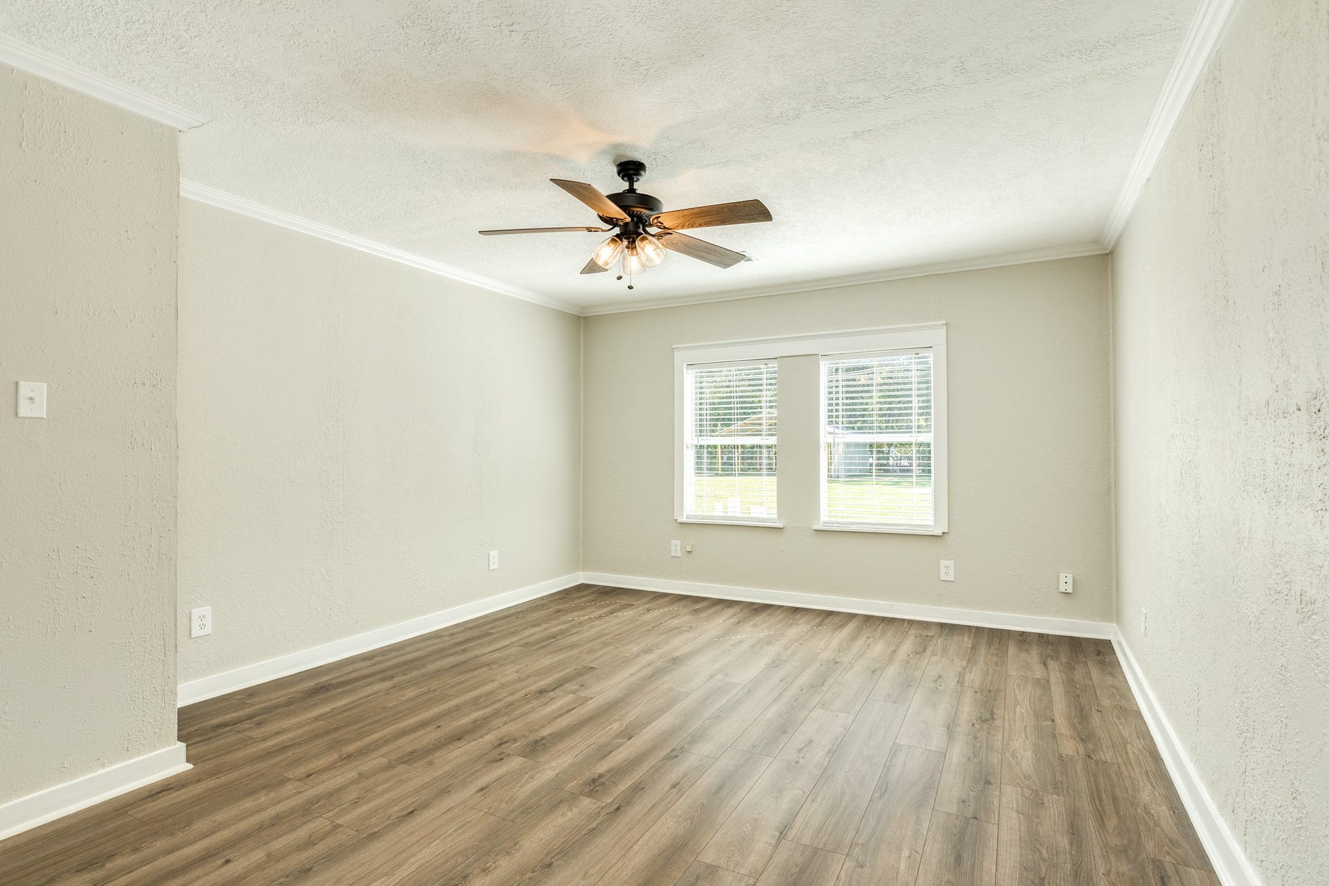 1602 County Road 939, Sweeny, TX 77480 Generously sized bedroom features wood-look flooring, neutral walls, crown molding, and a ceiling fan with lighting. Two windows welcome natural light and offer views of the surrounding greenery.