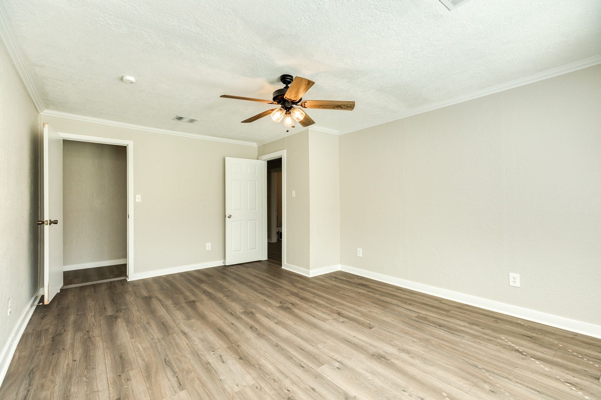 1602 County Road 939, Sweeny, TX 77480 Another view highlights the bedroom's spacious layout, wood-look flooring, and neutral finishes. A ceiling fan with lighting and convenient access to the closet and adjoining hallway complete the space.
