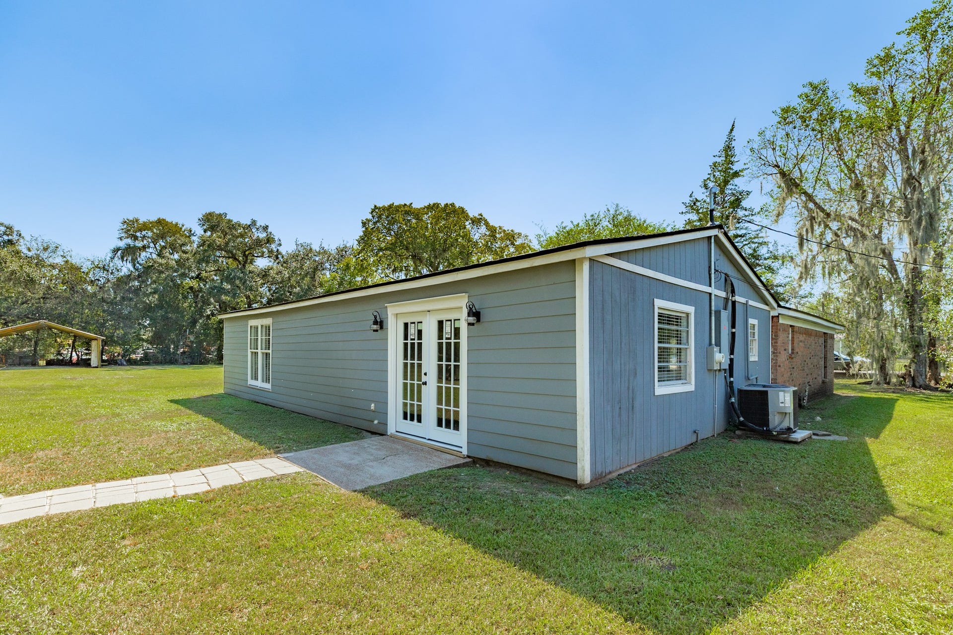 1602 County Road 939, Sweeny, TX 77480 Rear view showcases blue-gray siding, white-trimmed French doors, exterior lighting, and a concrete landing. The adjoining lawn offers easy access to the home's outdoor gathering areas.